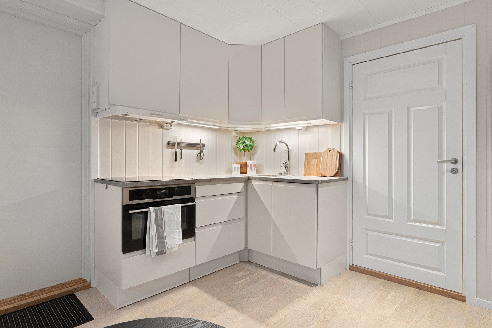 Kjøkkenet har innredning med glatte fronter og benkeplaten er av laminat. Det er integrert smal oppvaskmaskin, induksjonstopp og stekeovn.