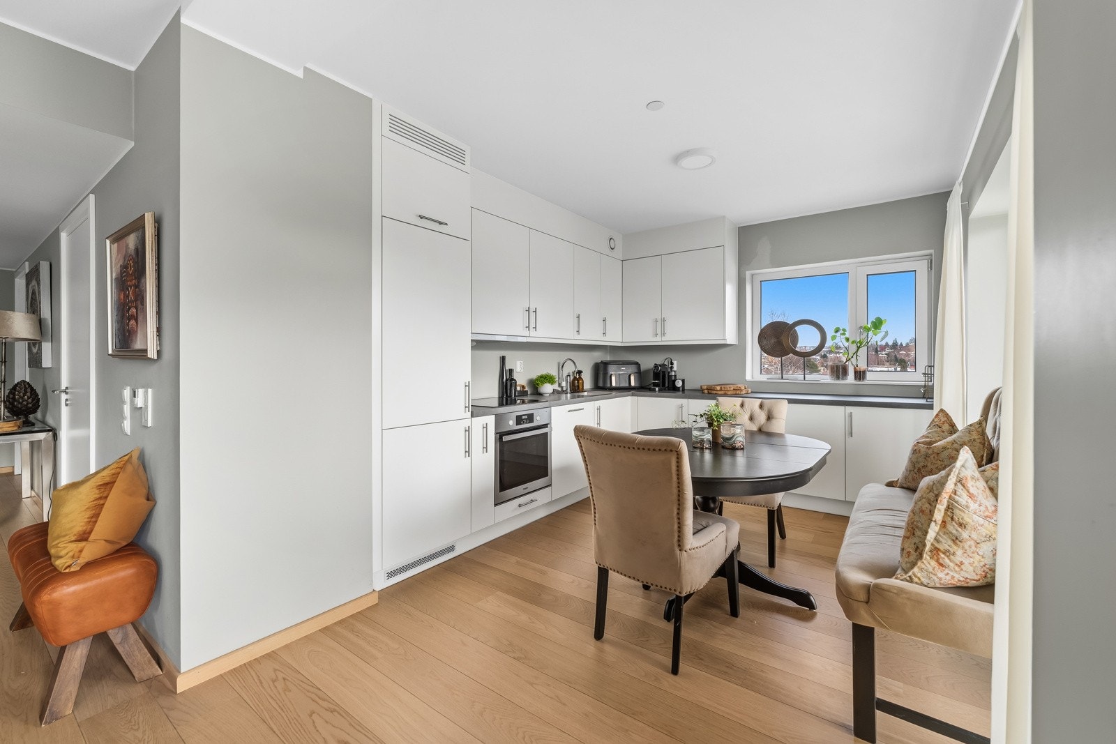 Dette gir god arbeidsflyt, et skreddersydd uttrykk og rikelig med skapplass. Innredningen har hvite, glatte fronter med stålhåndtak og benkeplate i grå laminat med planlimt vaskekum i stål. Galleribilde