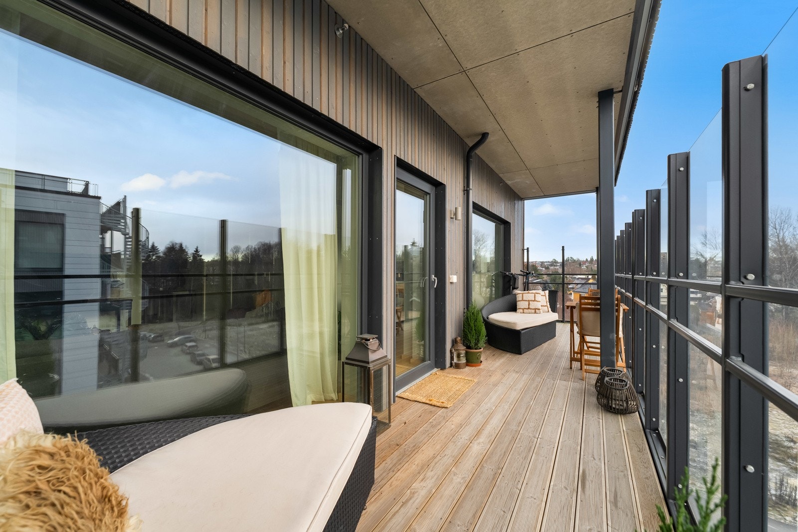 Uteplassen har dekke av terrassebord og høyt rekkverk i glass med sorte stolpe Galleribilde