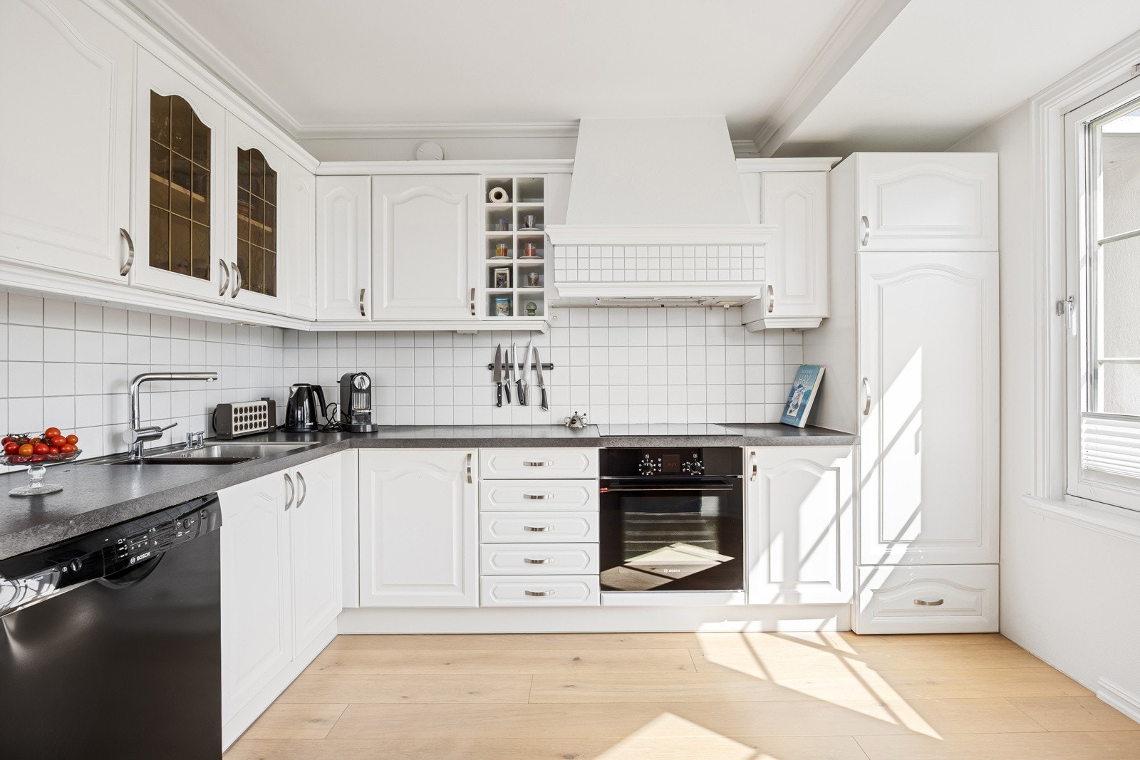 Benkeplaten er i grå laminat, og det er lagt hvite fliser over hele benken. Stekeovn og platetopp er integrert. Galleribilde