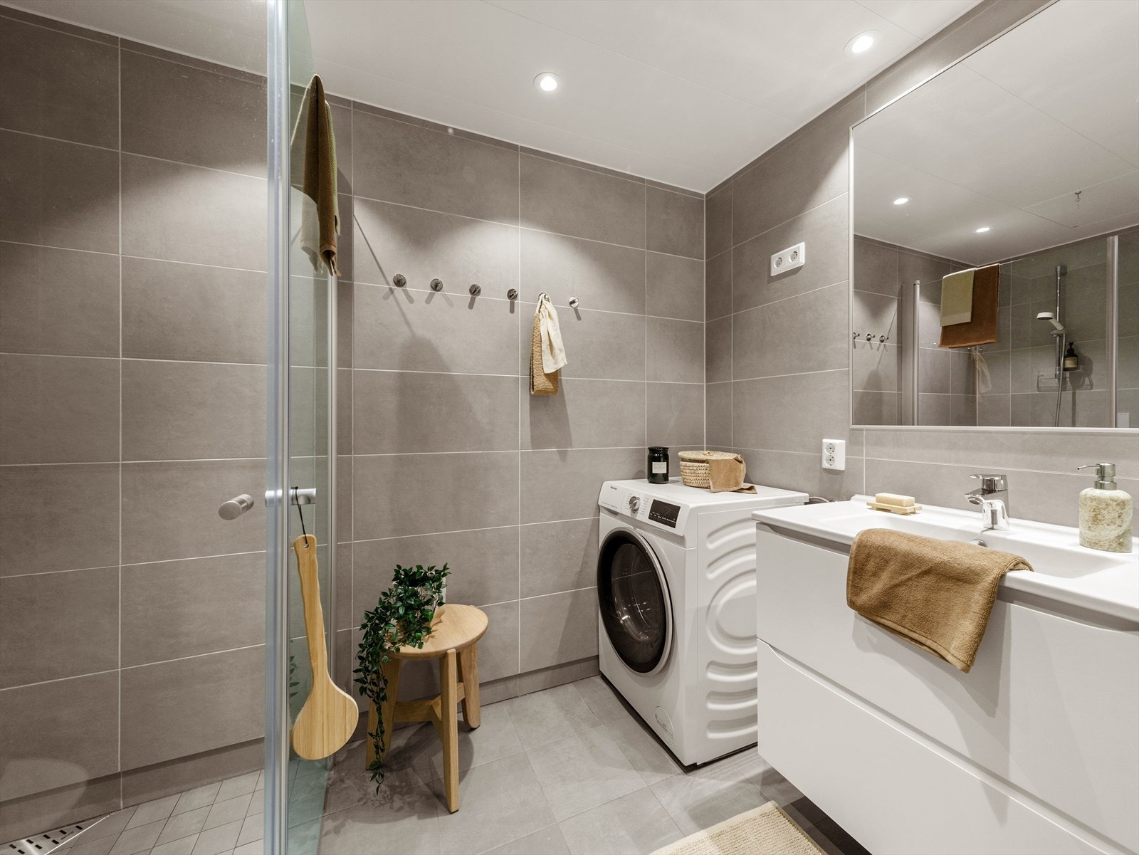 Pent helfliset bad innredet med baderomsinnredning med servant, vegghengt toalett, dusj og opplegg for vaskemaskin. Galleribilde