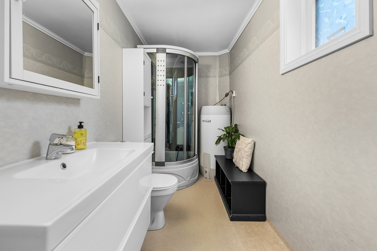 Våtrom med varme i gulv. Baderommet er innredet med servant med underskap, speil med tilhørende beslysning, dusjkabinett, gulvmontert toalett og opplegg for vaskemaskin. Galleribilde