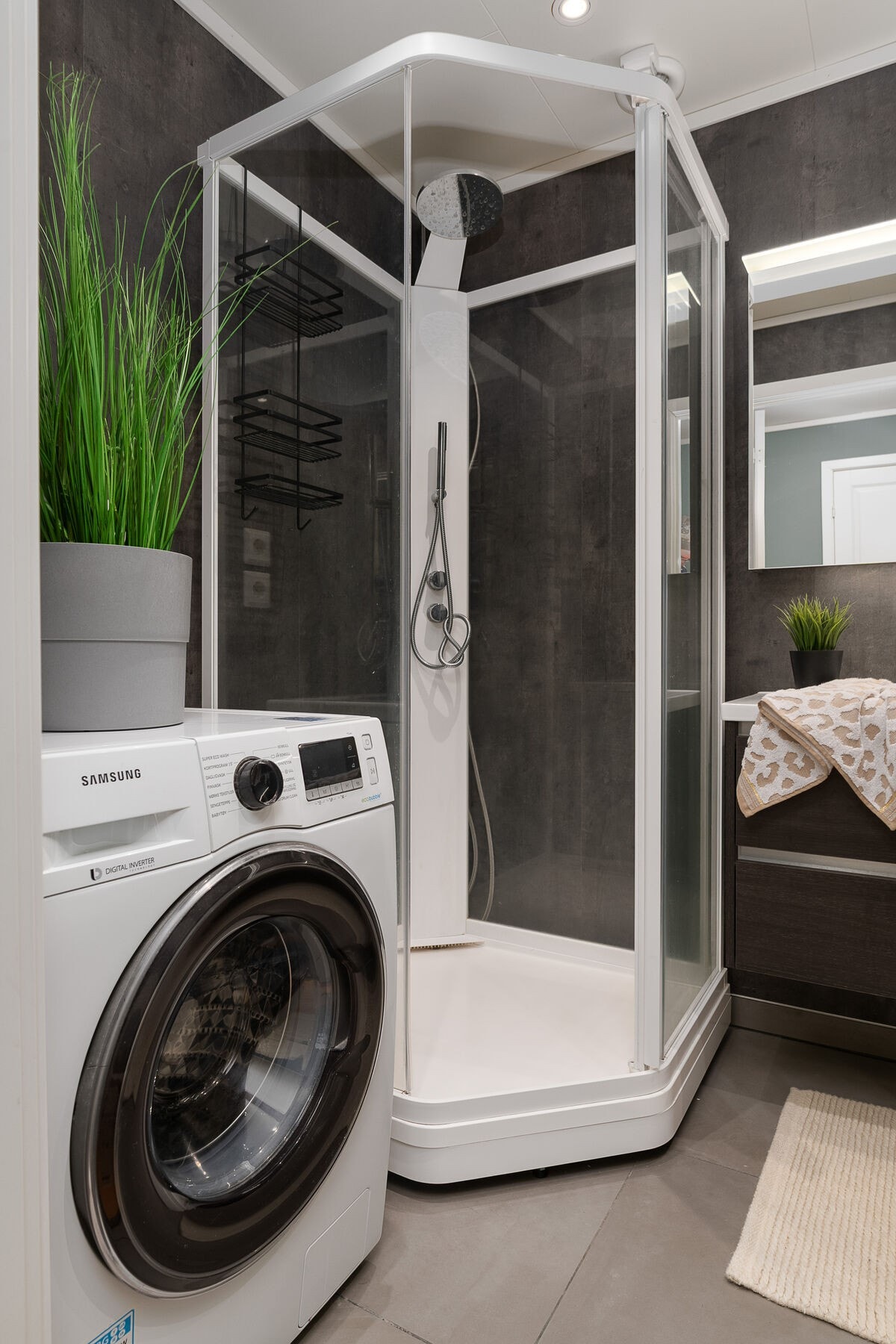 Badet har moderne baderomsplater på veggene, spotter i taket og flislagt gulv med elektriske varmekabler. Innredning med servant, veggmontert wc, dusjkabinett og opplegg for vaskemaskin. Galleribilde