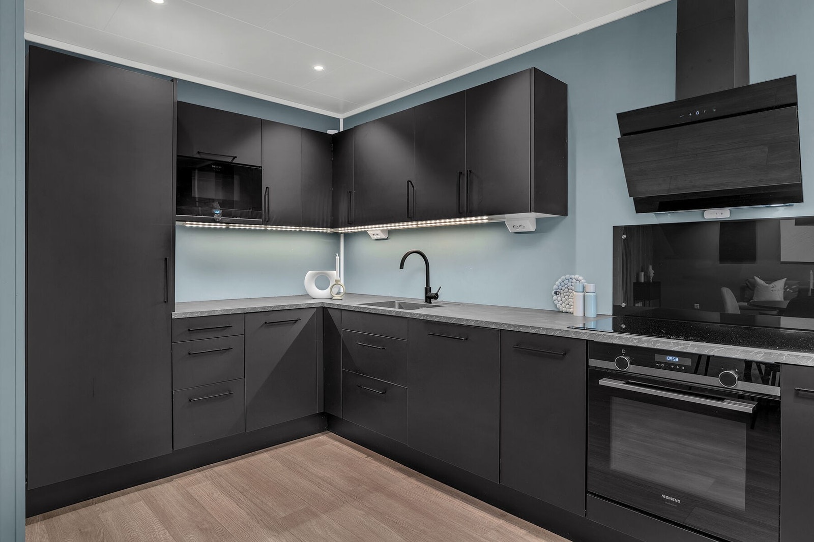 Stilrent kjøkken med sorte, glatte fronter og integrerte hvitevarer bestående av stekeovn, platetopp, kjøl/frys, oppvaskmaskin og micro. Galleribilde