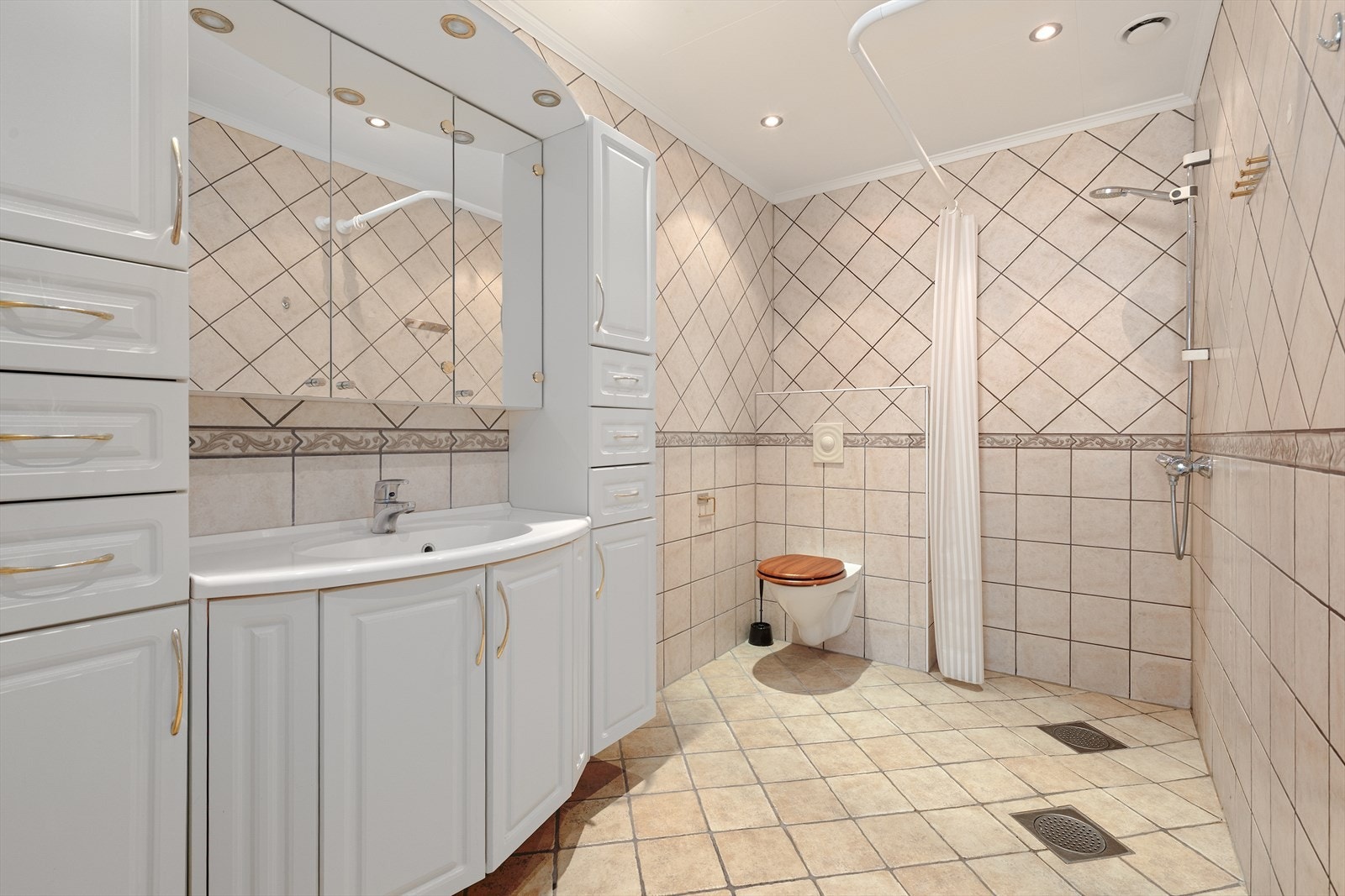 Romsleg bad med stor innreiing med benkeskap, høgskap på begge sider, samt dusj med forheng. Varmekablar i golv. Galleribilde