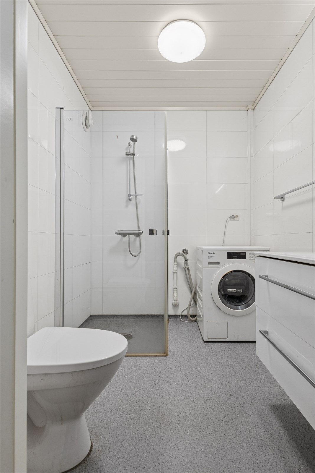 Baderommet er innredet med servant med skuffer, dusjhjørne , gulvmontert toalett og opplegg for vaskemaskin. Galleribilde