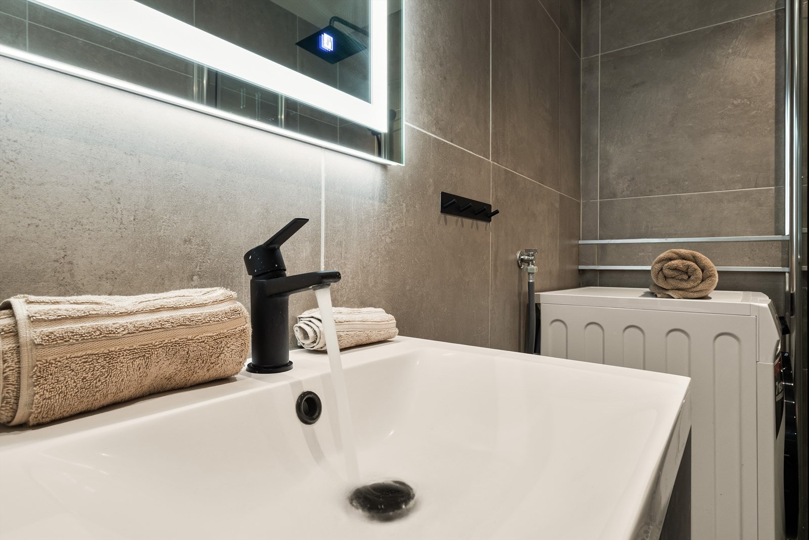 Rommet er innredet med servant med møblement og speil med belysning, toalett, dusjgarnityr og innfellbart dusjhjørne, samt opplegg for vaskemaskin Galleribilde