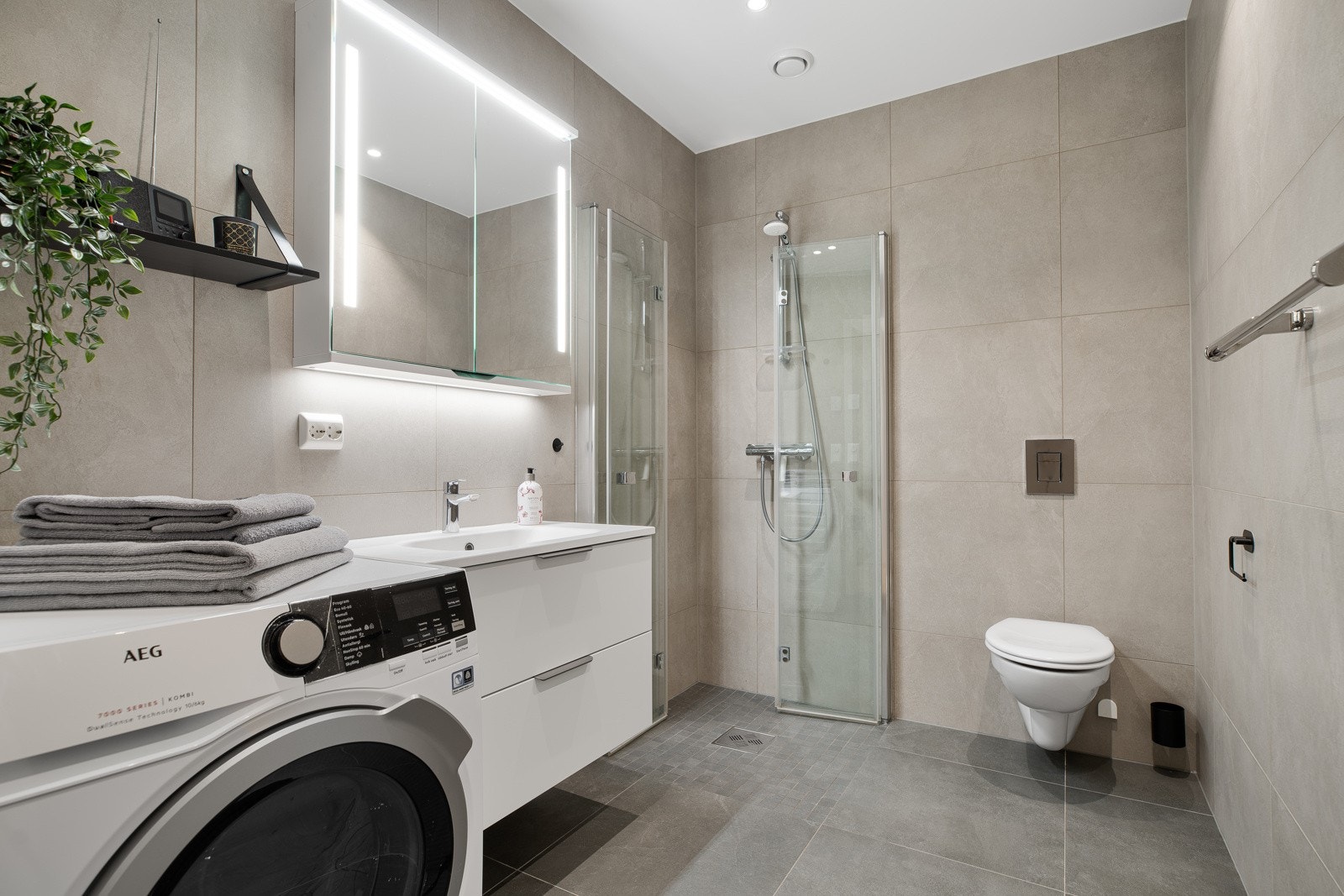 Lekkert bad med 60x60 fliser og innredning med skapplass, samt opplegg for vaskemaskin og plass til tørketrommel Galleribilde