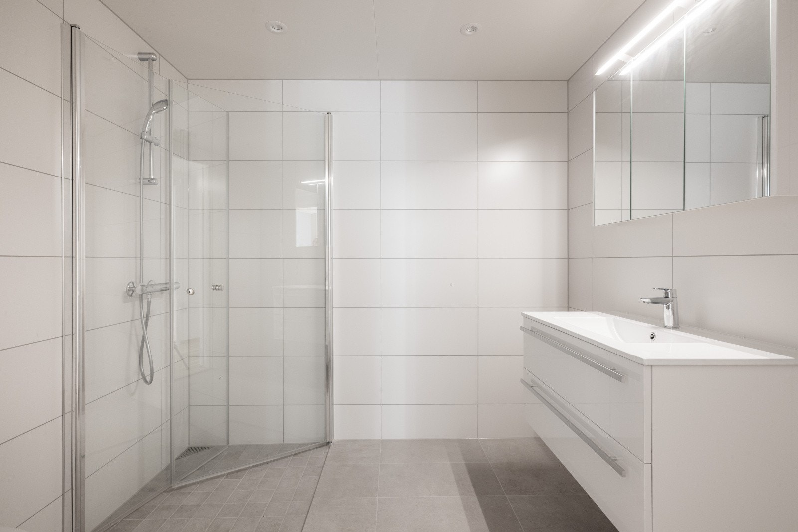 Pent, helfliset bad med gulvvarme og downlights i tak. Badet er innredet med veggmontert toalett, dusj med dusjvegger og servantinnredning med skuffer og speil. Det er balansert ventilasjon. Galleribilde