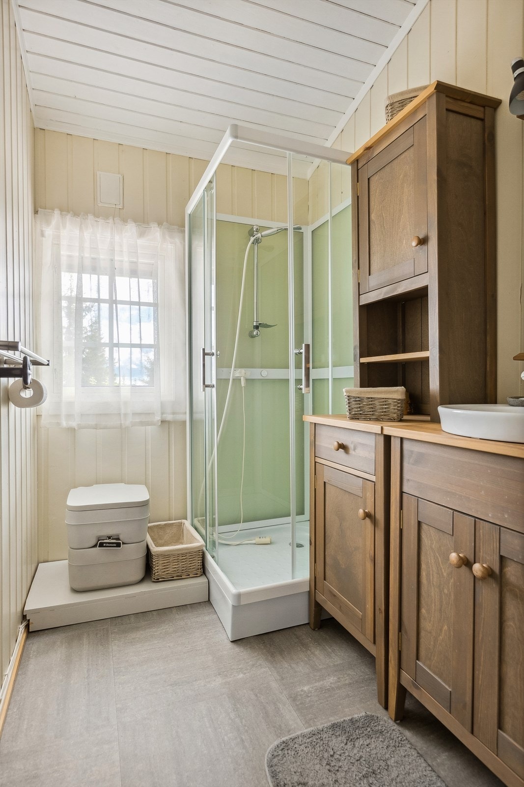 Enkelt hyttebad med belegg på gulvet og beiset innredning med integrert servant. Rommet har dusjkabinett og Porta Potti. Galleribilde