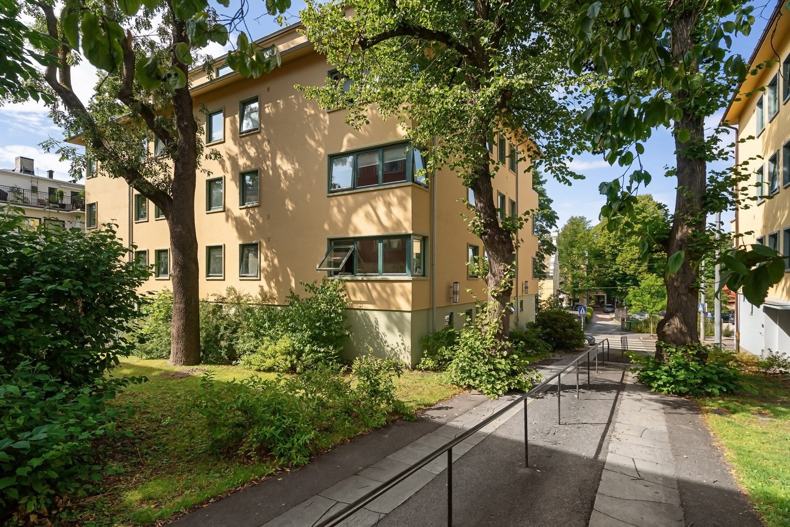 Velholdt bygård omkranset av frodig beplantning og store trær, som gir et grønt og skjermet bomiljø Galleribilde