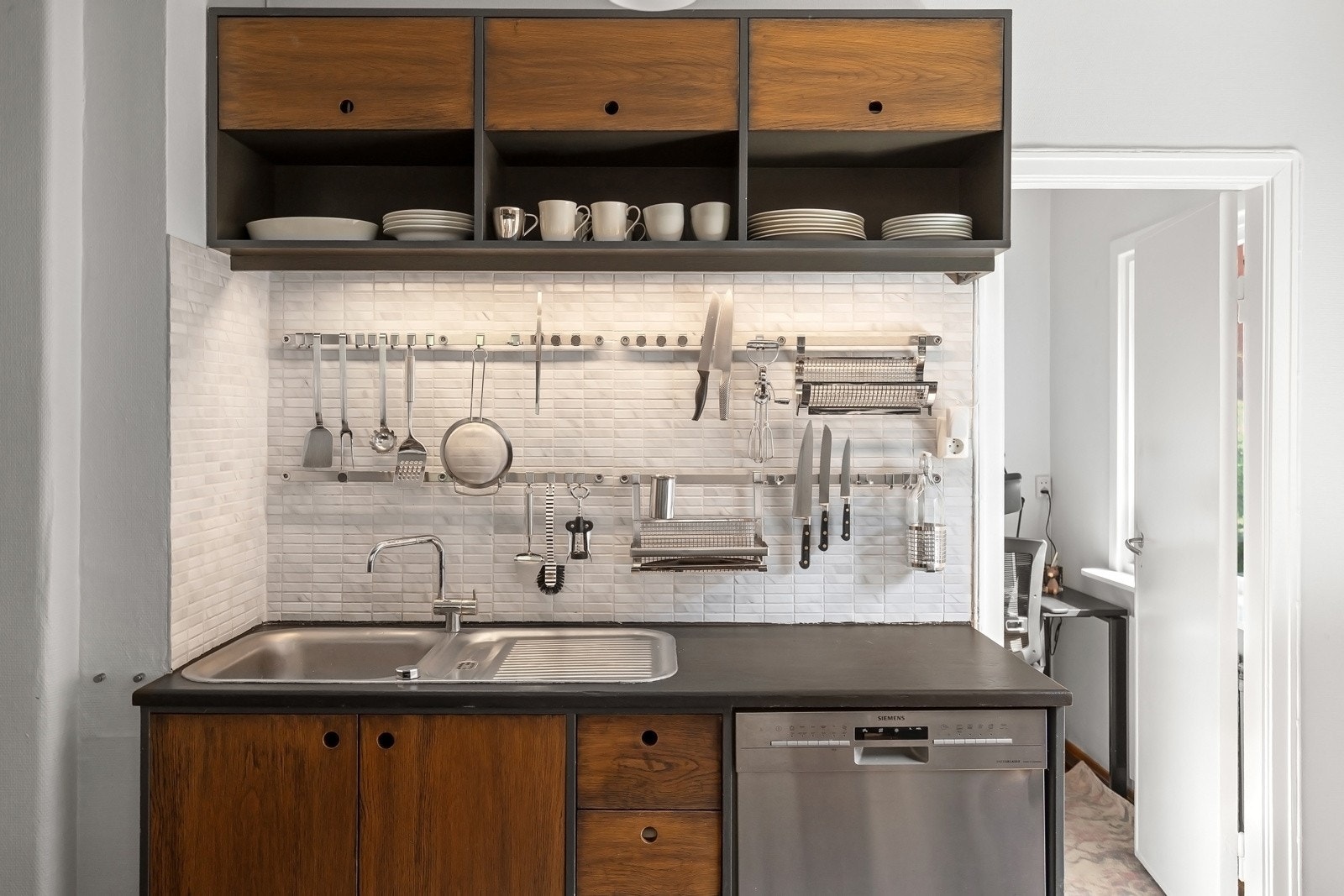 Plassbygget kjøkken innredet med slette fronter i finér, LED-belysning under overskap og heltre benkeplate med nedfelt stålkum Galleribilde