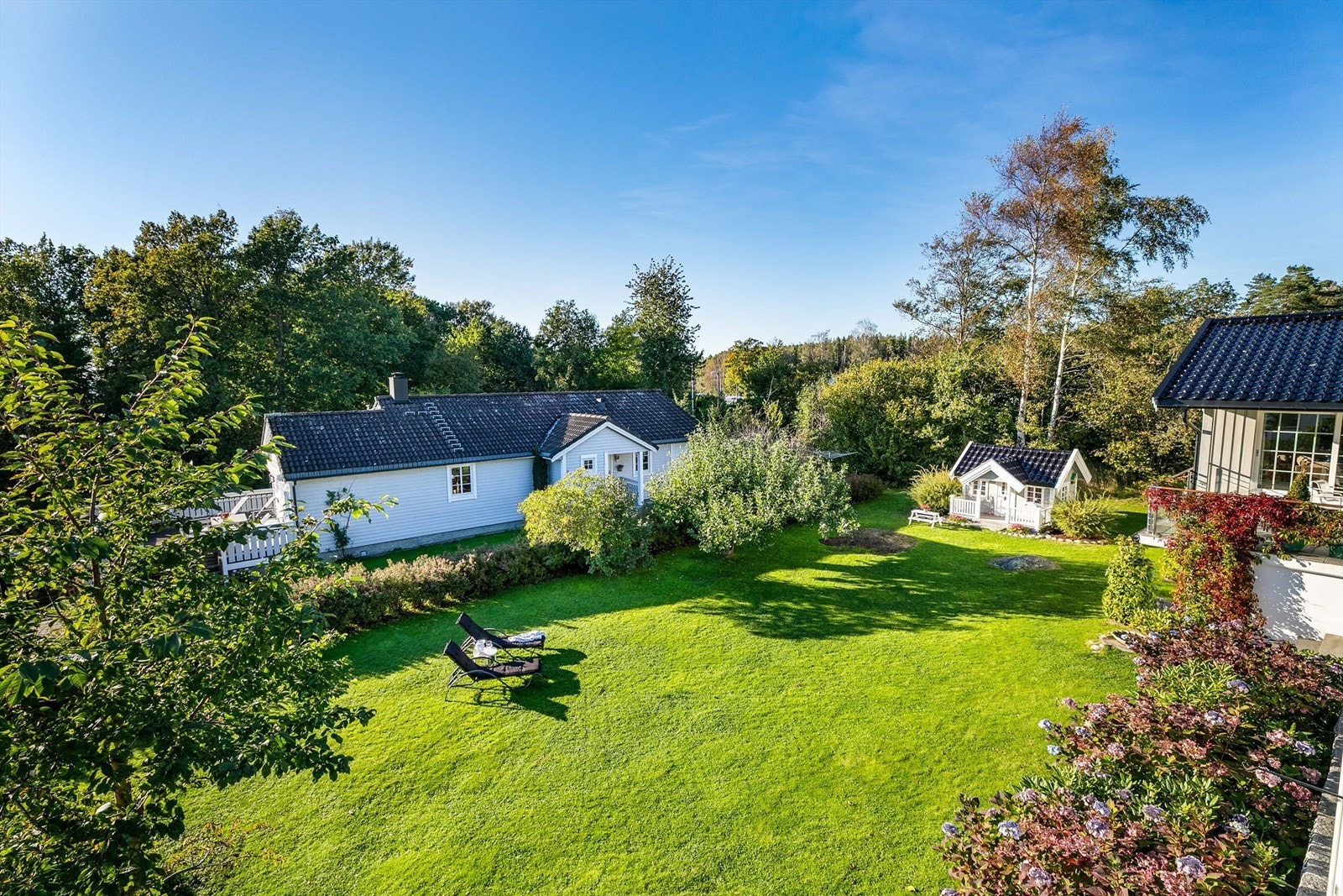 Utsyn fra terrassen over hagen der store og små får masse tumleplass. Lekestuen er oppført i samme stil som boligen. Galleribilde
