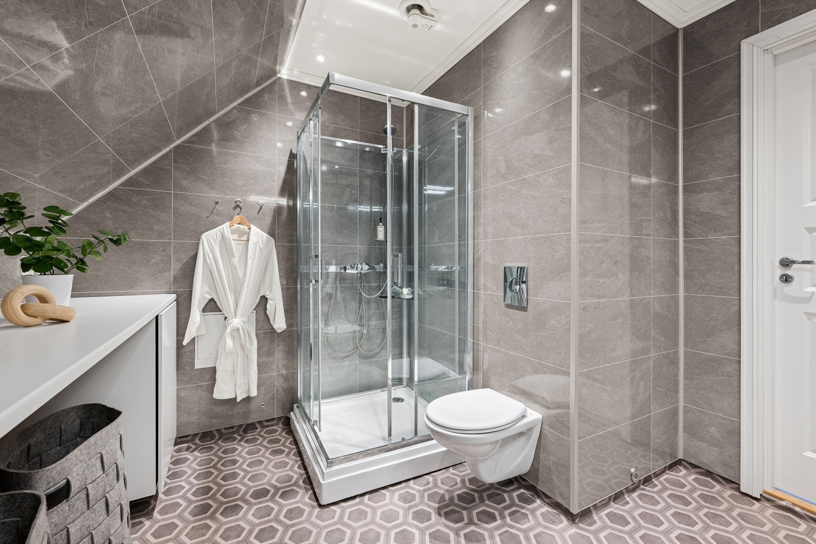 Badet ble pusset opp i 2020 og er innredet med grått, mønstrete vinylbelegg på gulv og grå baderomsplater på vegg. I gulvet har man også varmekabler for ekstra komfort. Galleribilde