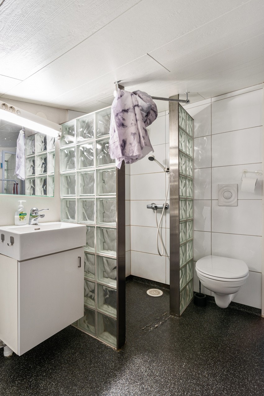 Baderommet er utsyrt med vegghengt toalett, dusjhjørne og servant med underskap.