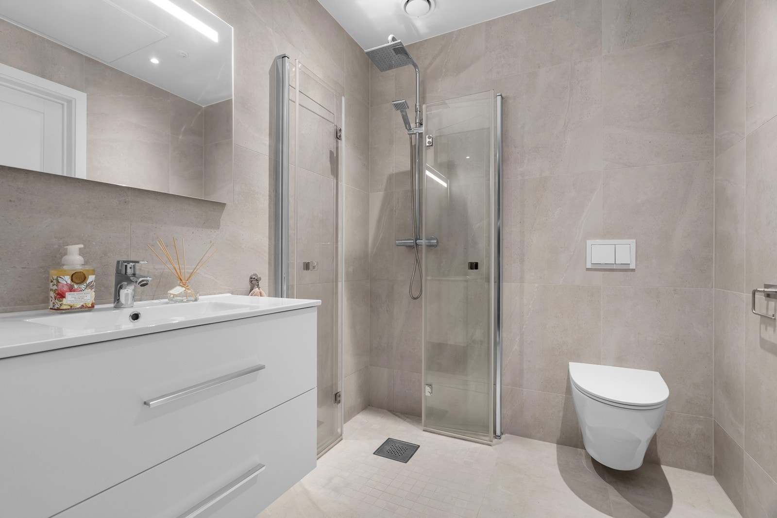 Badet er innredet med nedfelt servant, vegghengt toalett og dusjhjørne med innfellbare dører Galleribilde