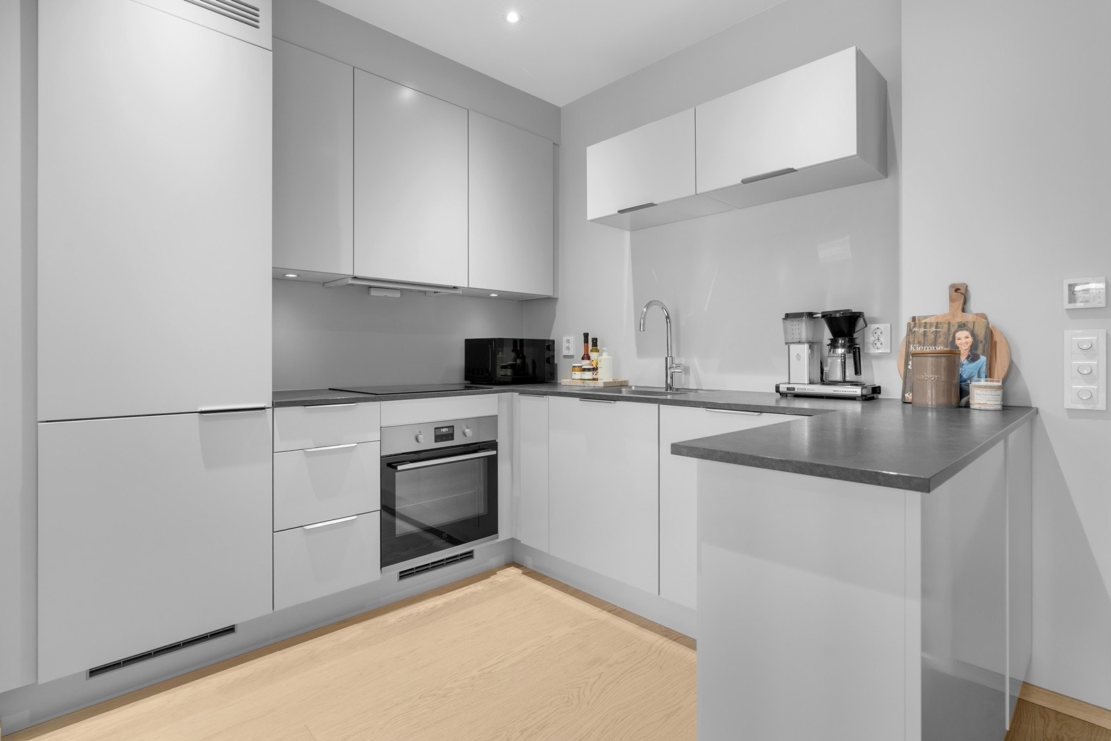 Lekkert kjøkken bestående av integrerte hvitevarer, nedfelt vask og platetopp. Galleribilde