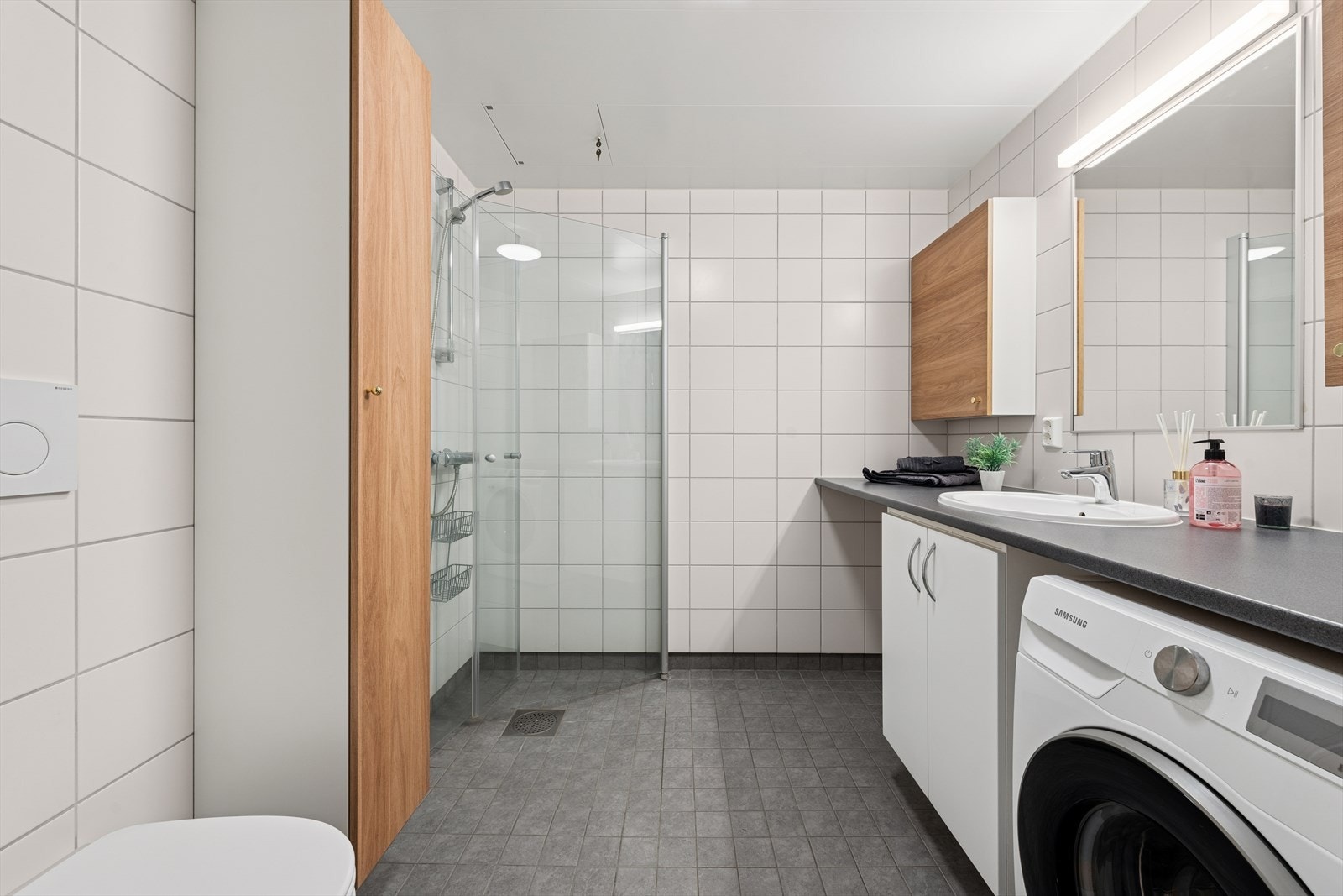 Badet er av god størrelse, og byr på vegghengt wc, dusj med innfellbare glassdører, servant med underskap og opplegg til vaskemaskin. Det er ellers godt med lagring i vegghengte baderomsskap. Galleribilde