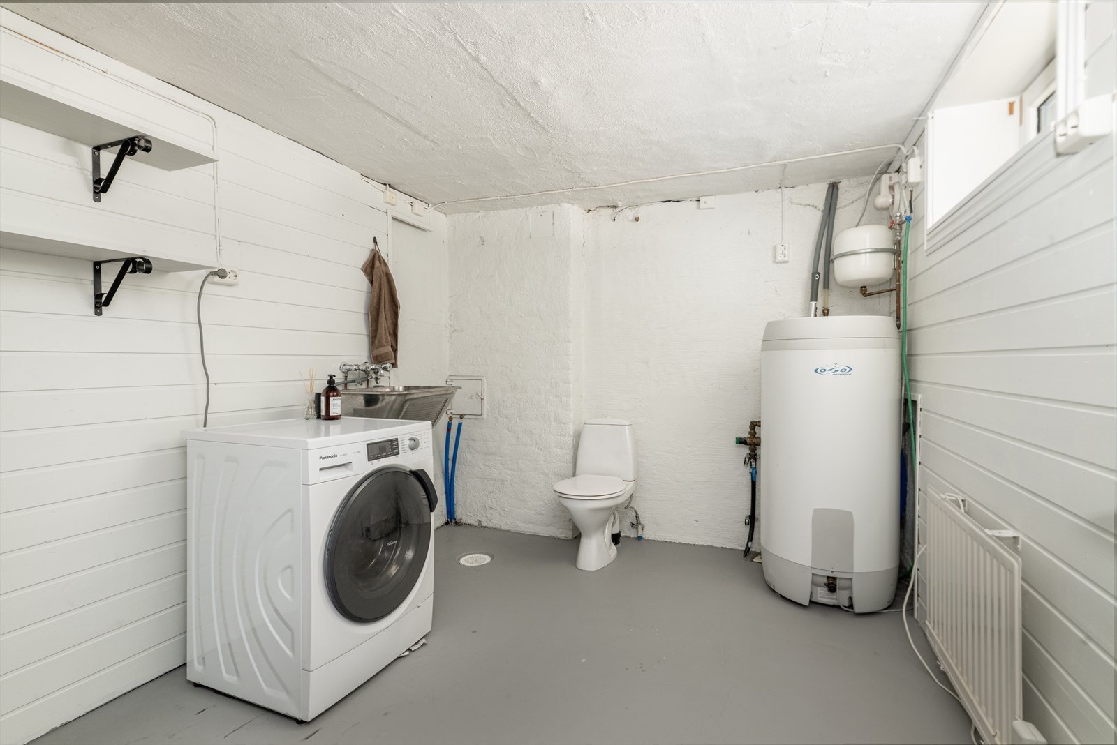 Vaskerommet i kjeller med malt betonggulv, og malte overflater. Dette rommet innehar skyllekar i stål og toalett. Det er opplegg for vaskemaskin og tørketrommel. Galleribilde