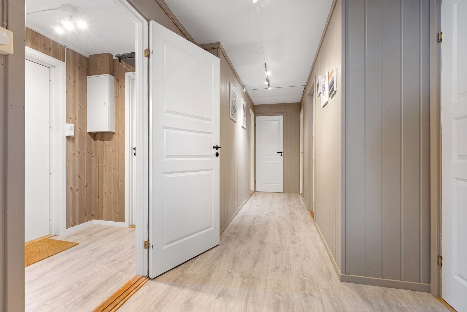 Den brede gangen gir en åpen og god flyt mellom rommene, og detaljene i panel og belysning skaper en varm, gjennomført atmosfære. Galleribilde