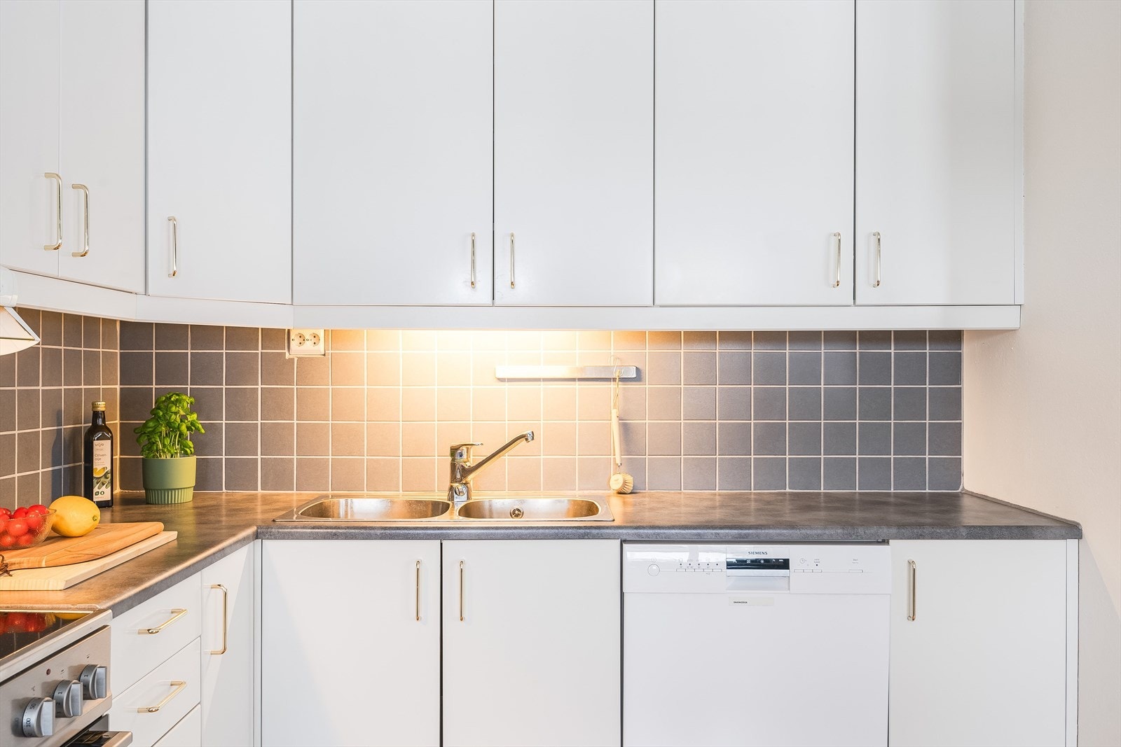 Praktisk med fliser i benkeryggen og belysning under de takhøye overskapene. Galleribilde