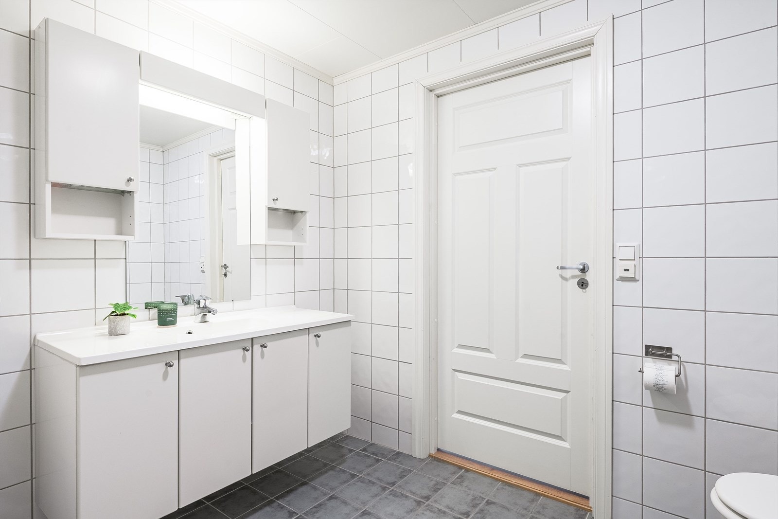 Baderommet har grå fliser på gulv med gulvvarme, hvite fliser på veggene og mekanisk avtrekk. Galleribilde