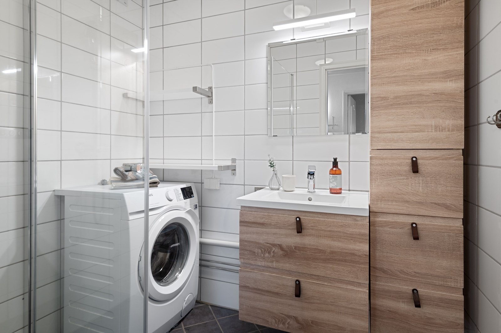 Flislagt baderom med varme i gulv. Rommet er innredet med servant med underskap, dusjvegger og opplegg for vaskemaskin. Galleribilde