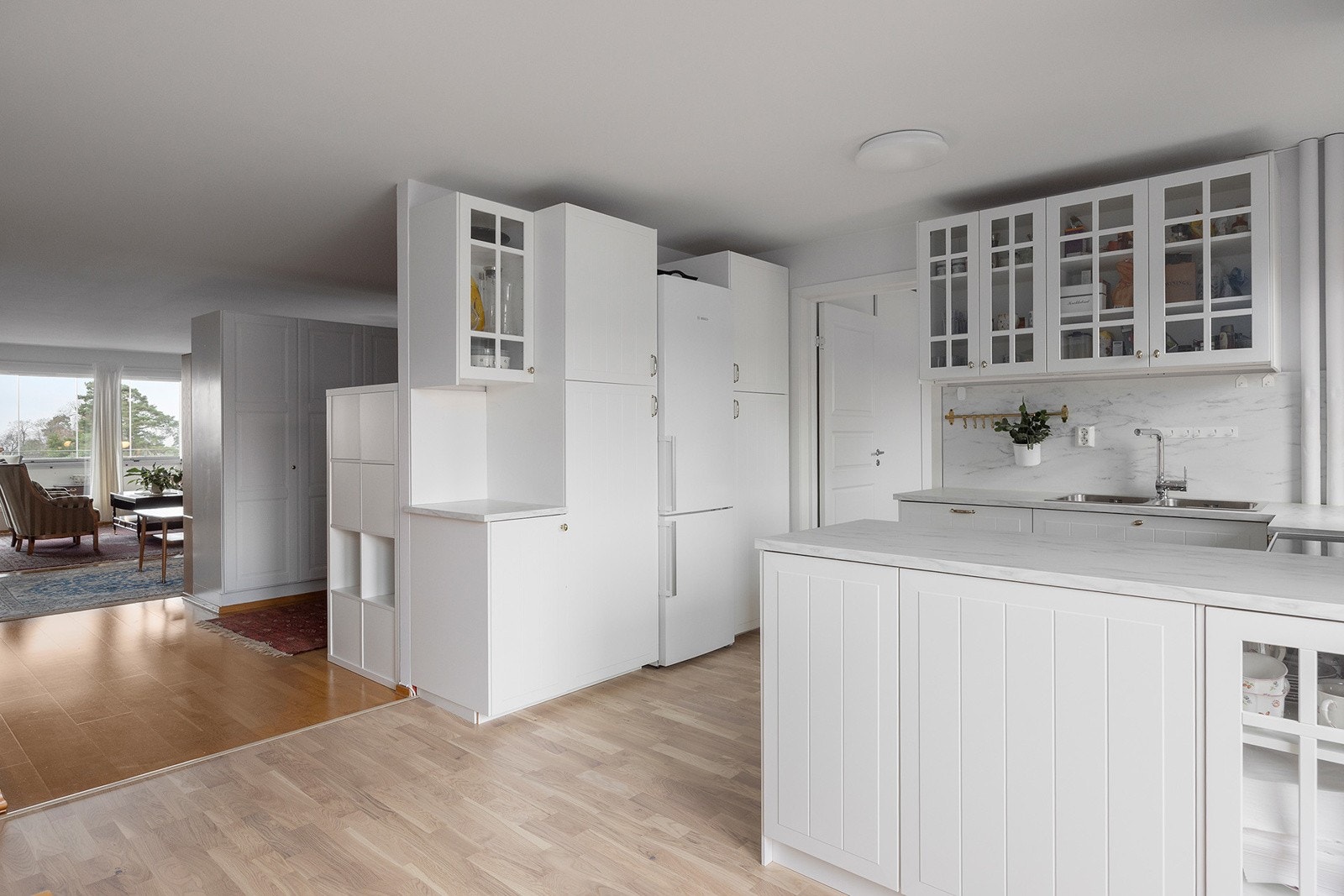 IKEA kjøkkeninnredning med glatte folierte skapfronter, laminat benkeplate med sprutplate på bakvegg, høyskap, dobbel oppvaskkum, ventilator og innfelte hvitevarer som oppvaskmaskin, frittstående komfyr, kjøl/- fryseskap Galleribilde