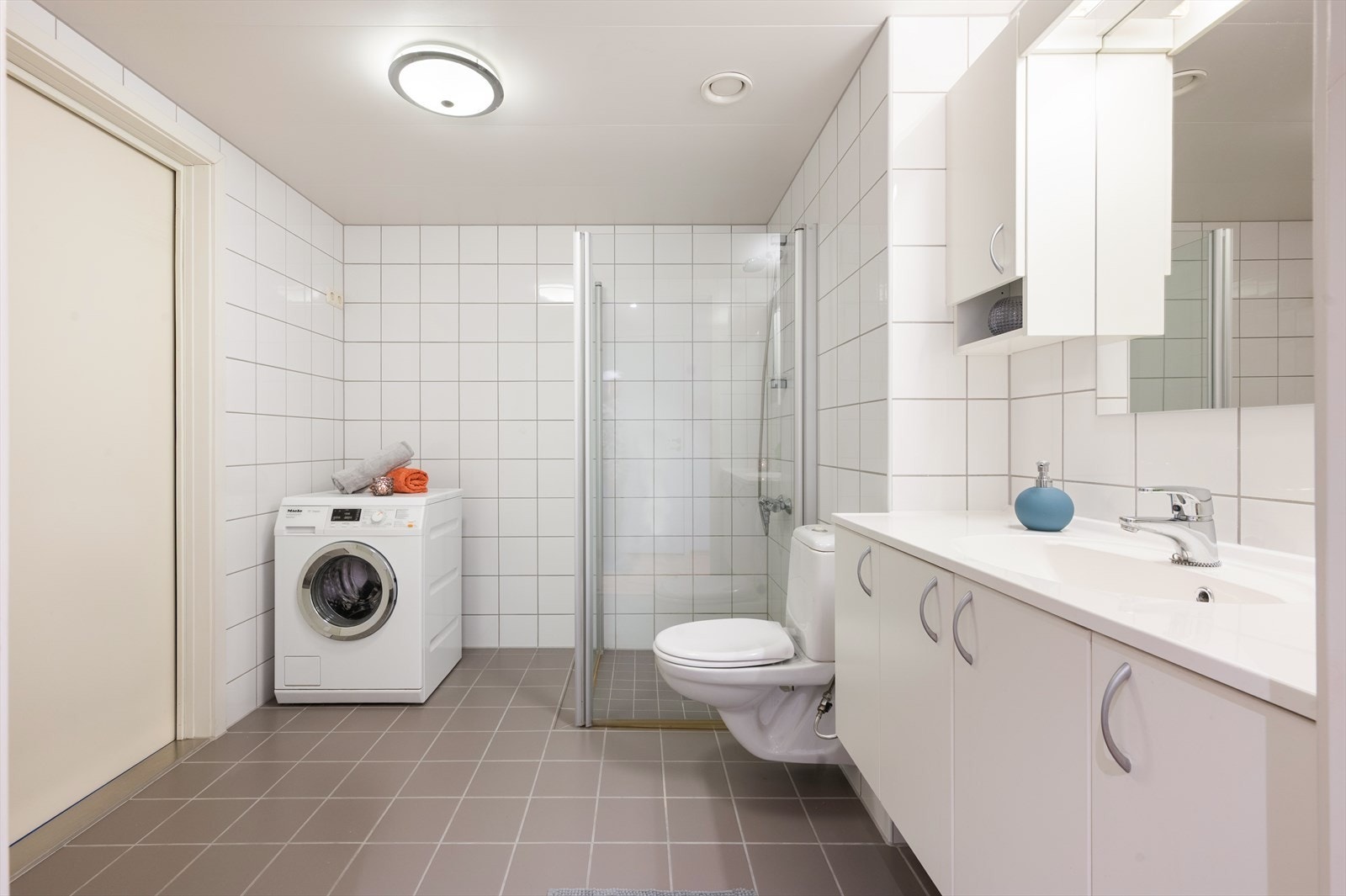 Badet er videre innredet med stor servantinnredning med gode oppbevaringsmuligheter, vegghengt speil og skap. Opplegg for vaskemaskin og tørketrommel. Galleribilde