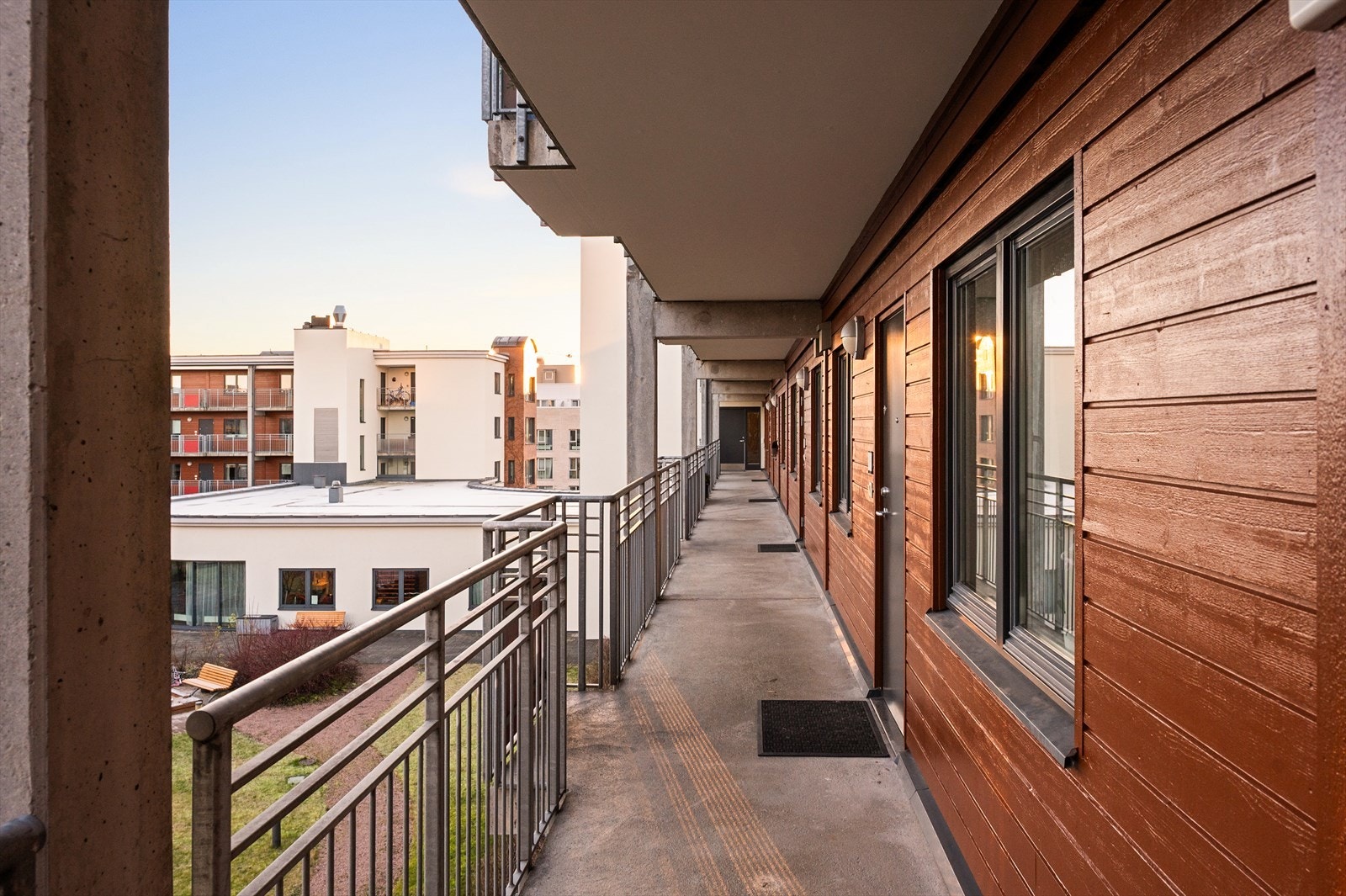 Hyggelig inngangsparti via svalgang. Her ser man ned til borettslagets felles bakgård som er pent opparbeidet. Det hvite bygget er serviceområdet til Selvaag Plus konseptet. Galleribilde