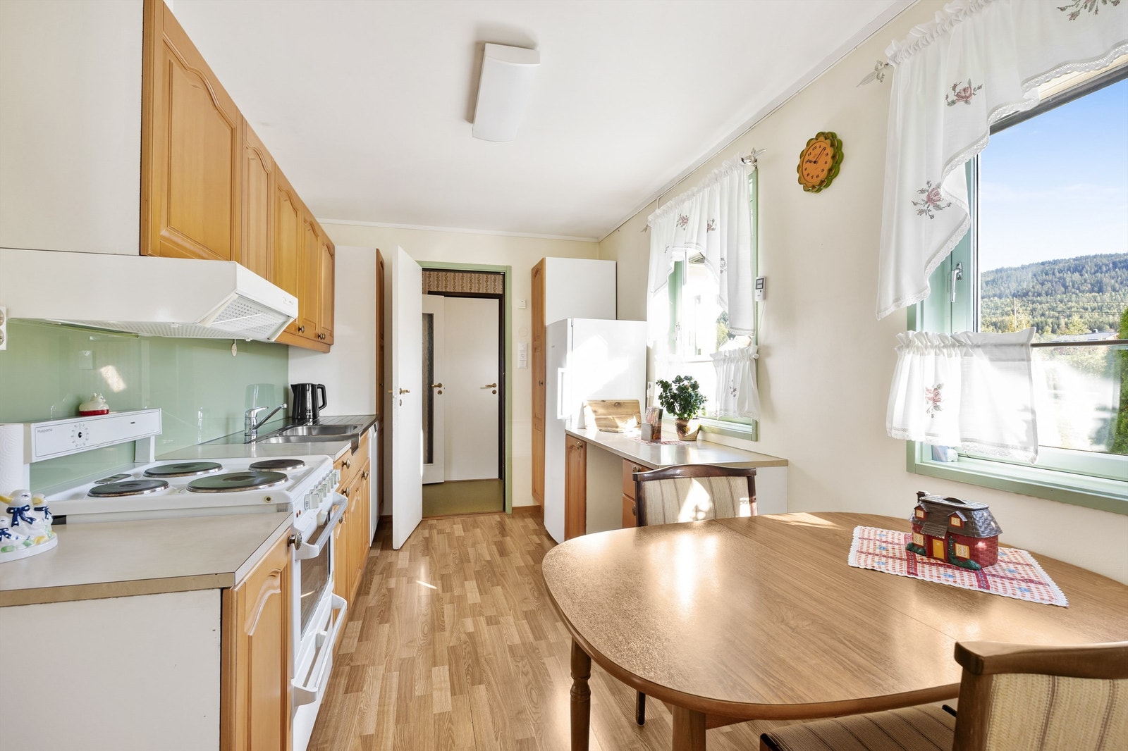 Kjøkken av eldre dato. Innredningen består av profilerte fronter, laminert benkeplate og benkebeslag i rustfritt stål. Det er belysning under overskapet. Hvitevarene er frittstående. Galleribilde