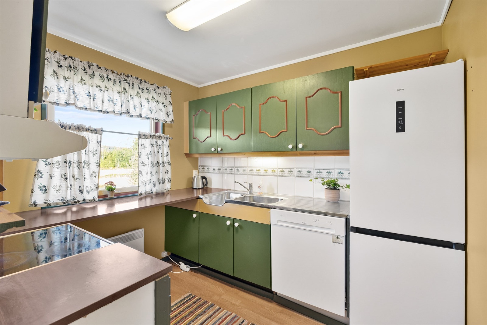 Kjøkkenet er av eldre dato. Innredningen består av profilerte og glatte fronter. Det er belysning under overskapet, fliser på vegg under overskapet. Galleribilde