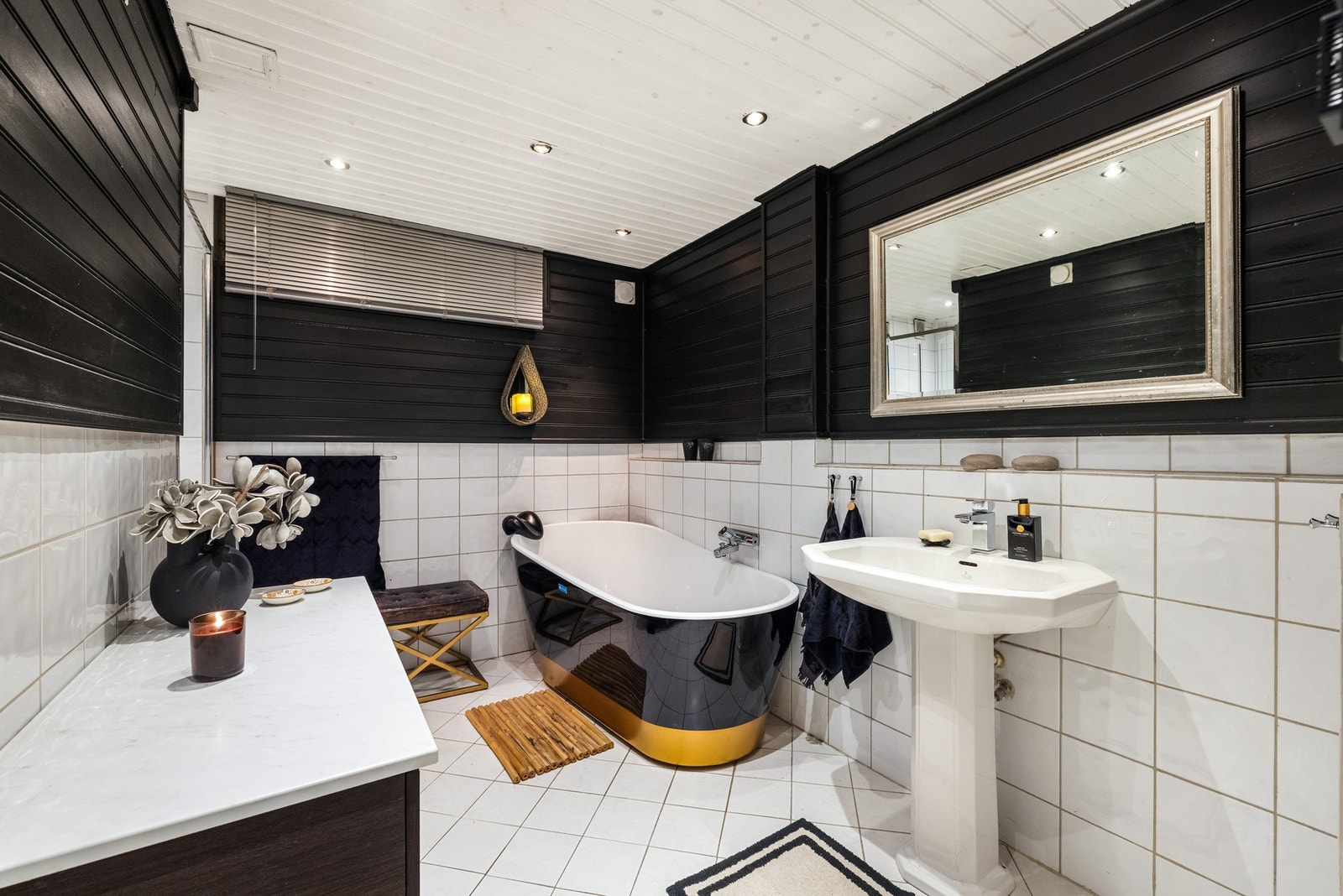 Baderommet i finner du i boligens underetasje. Badet har hvite fliser på gulvet, hvite fliser og sort panel på veggene, samt hvitmalt himling med downlights. Galleribilde