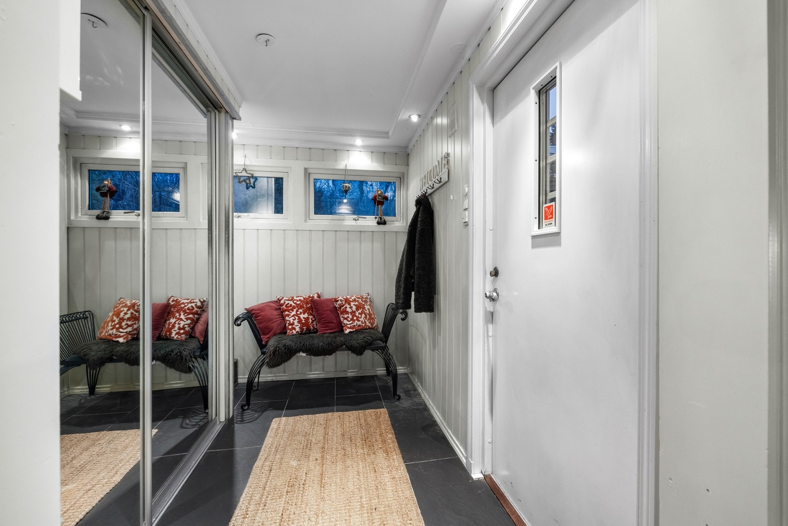 Her er det mørke fliser på gulvet med gulvvarme, hvitmalt panel på veggene og himling med downlights. Videre er det en stor skyvedørsgarderobe i entréen med speilflater som gir en følelse av et lysere og større rom. Galleribilde