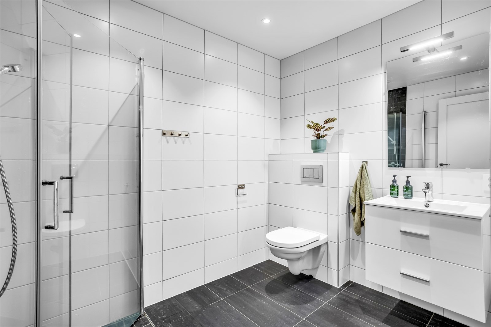 Delikat bad med gulvvarme og downlights i himling. Badet har hvit servantinnredning, speil, toalett og dusjhjørne. Galleribilde