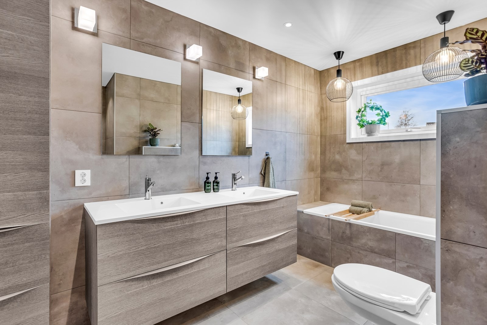 Badet har servantinnredning med skuffeseksjon, høyskap, speil, vegghengt toalett, dusjhjørne med glassdører og innebygd badekar. Galleribilde