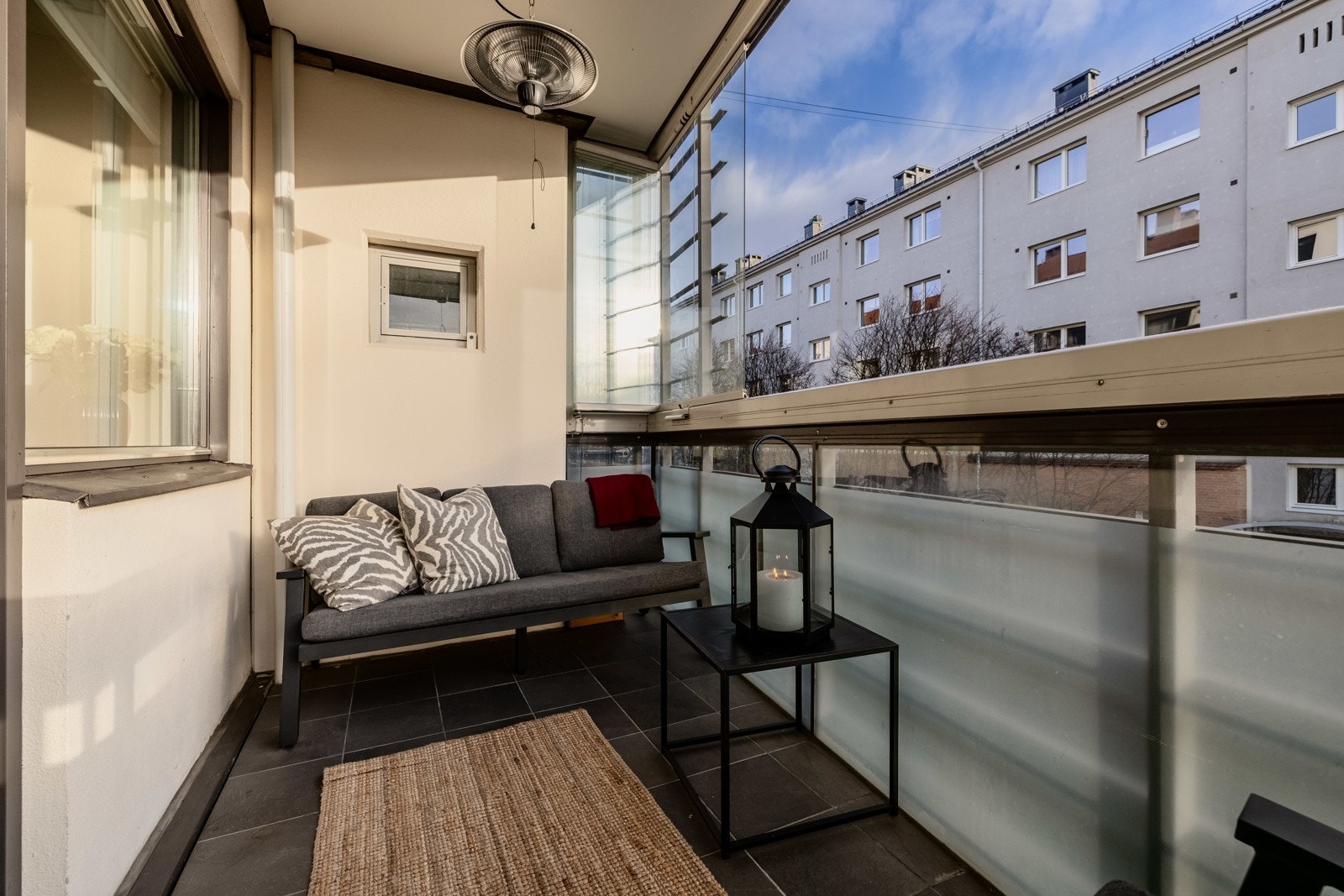 Balkongen har mørke fliser på gulv, rekkverk av metall og glass, samt glassfelt som kan åpnes helt opp. Det er også montert terrassevarmer, utebelysning og stikkontakt. Galleribilde