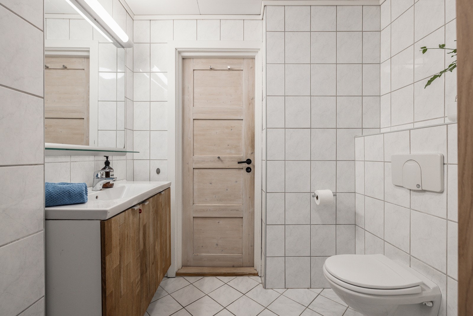 Baderomsinnredning med ovenpåliggende servant og speil med belysning over. Baderommet er også utstyrt med dusjhjørne med skyvedører av glass og vegghengt toalett. Galleribilde