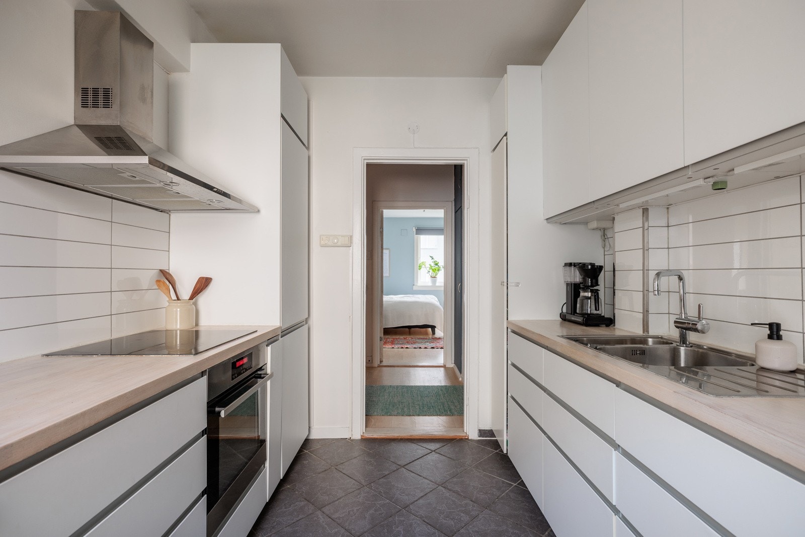 Innredningen har hvite glatte fronter og benkeplate av tre (slipt i 2022) med nedfelt oppvaskkum. Praktisk med lyse fliser i benkeryggen og belysning under overskapene. Galleribilde