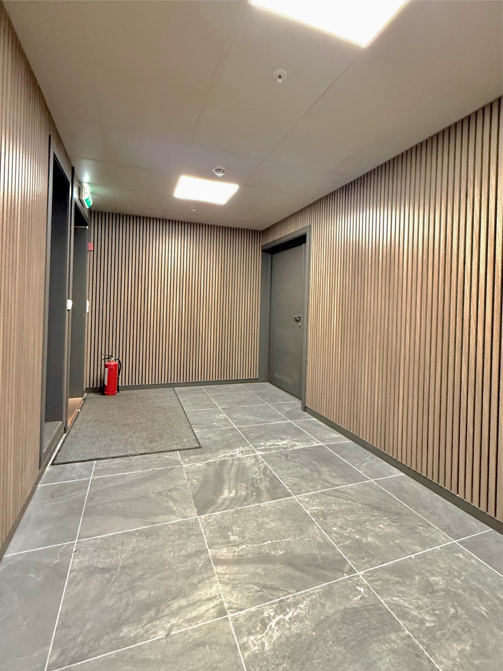 Pene fellesarealer med moderne trepaneler og flislagt gulv gir et godt førsteinntrykk før du går inn i leiligheten Galleribilde