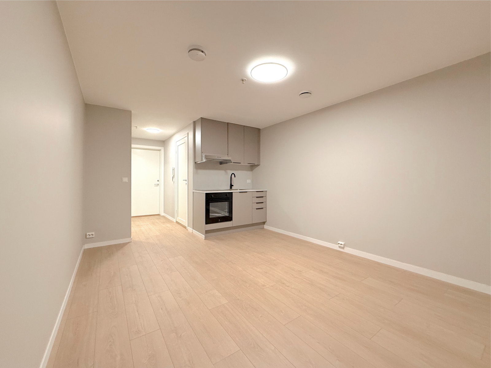 God romfølelse i stue/kjøkken området. Kjøkkenet ligger i bakkant, og inngangspartiet er synlig i enden av rommet Galleribilde