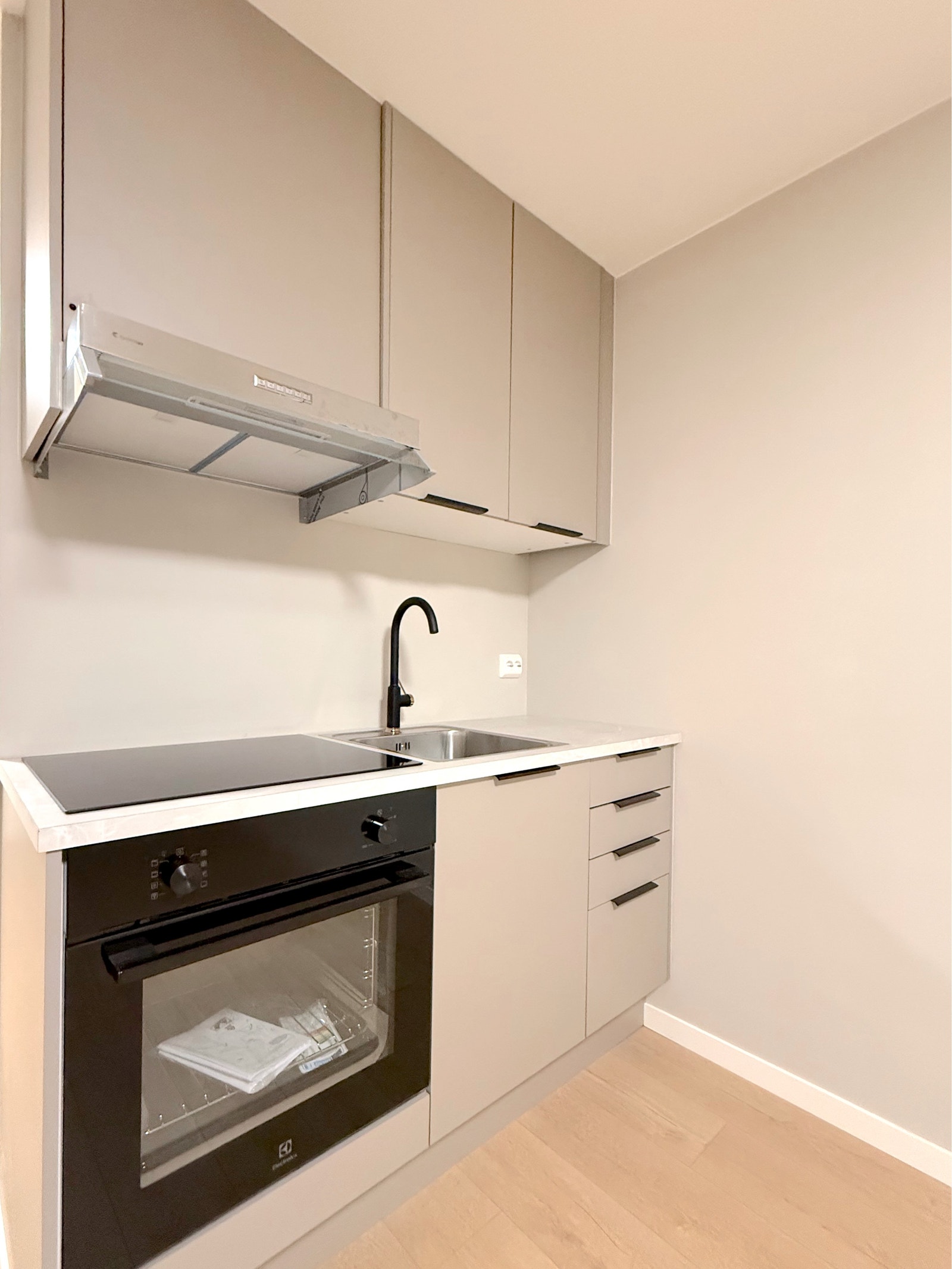 Detaljbilde av kjøkkenet med integrert stekeovn, platetopp, ventilator og vask med sort armatur Galleribilde