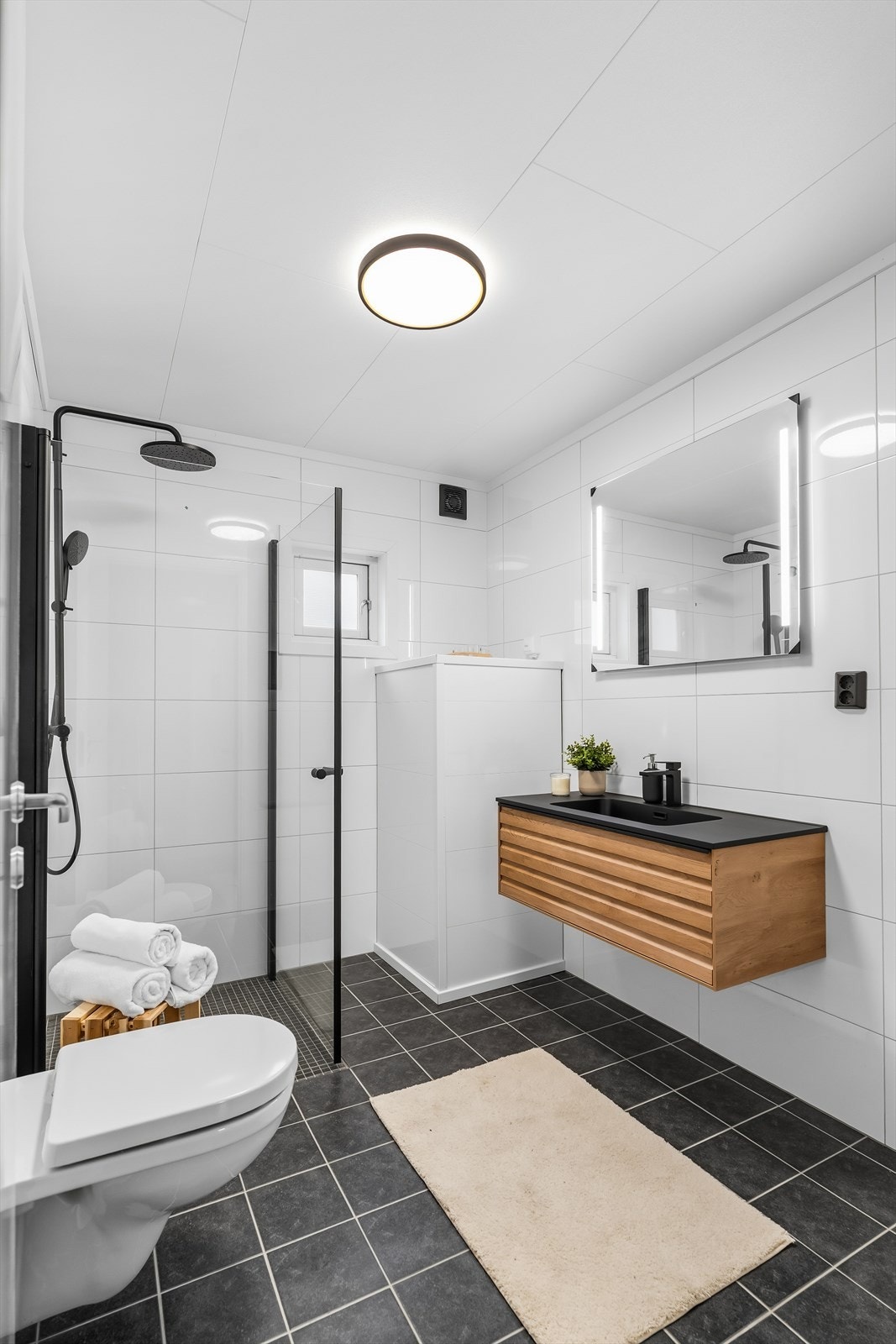 Oppusset bad som er helfliset med moderne innredning og intallasjoner, gjennomgående sorte detaljer. Galleribilde