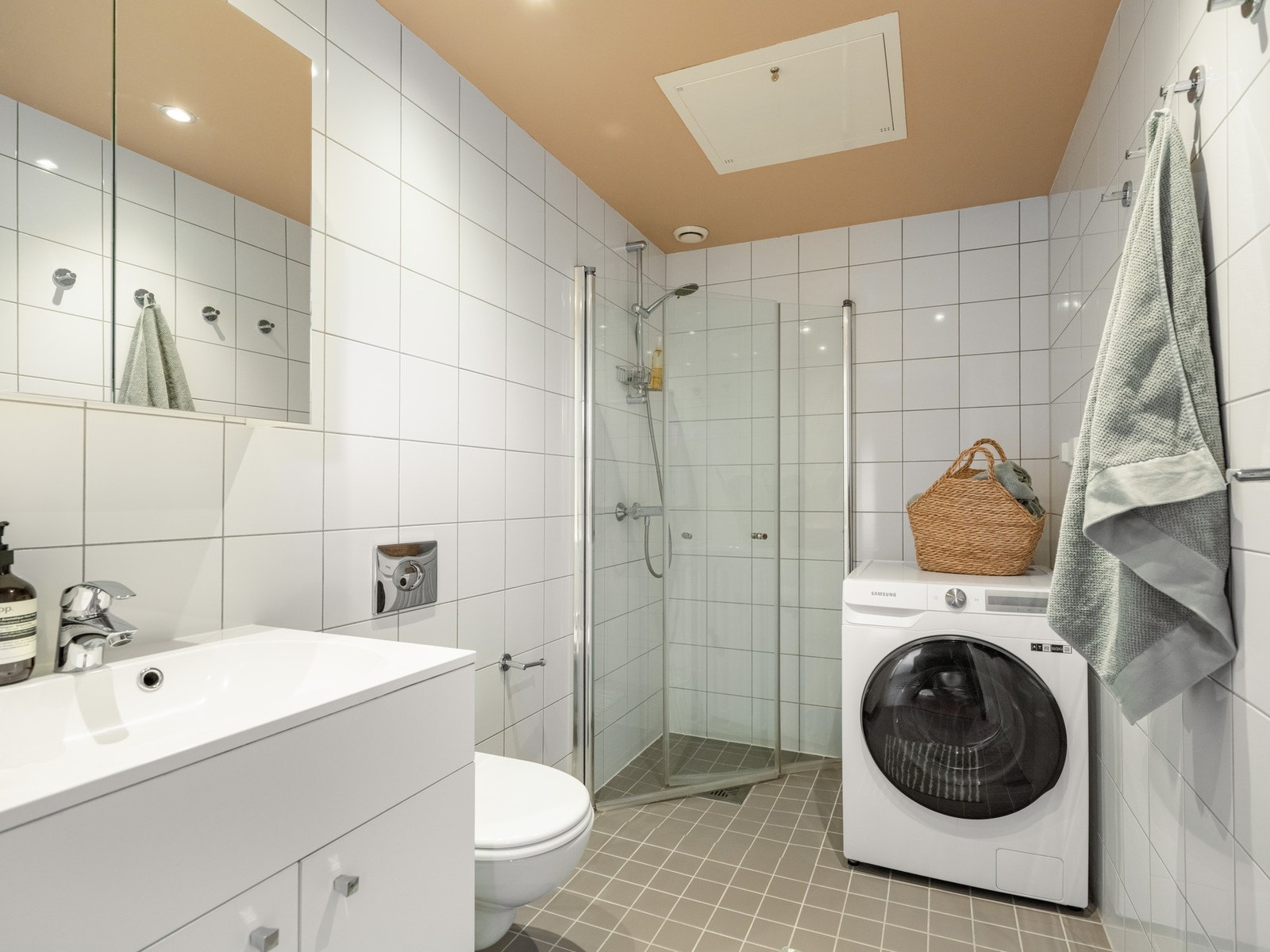 Her er det flislagte vegger og tak, vegghengt toalett, dusjhjørne, servant og opplegg til vaskemaskin. Galleribilde