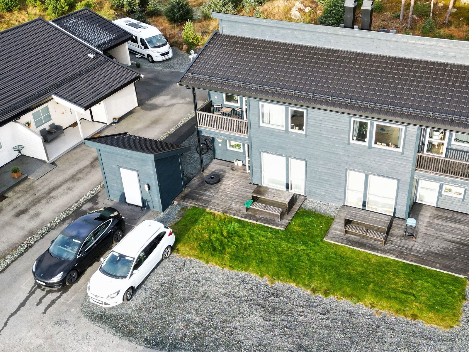 Luftfoto av bustaden med tilhøyrande terrasse, plen og gode parkeringsplassar rett utanfor. Galleribilde