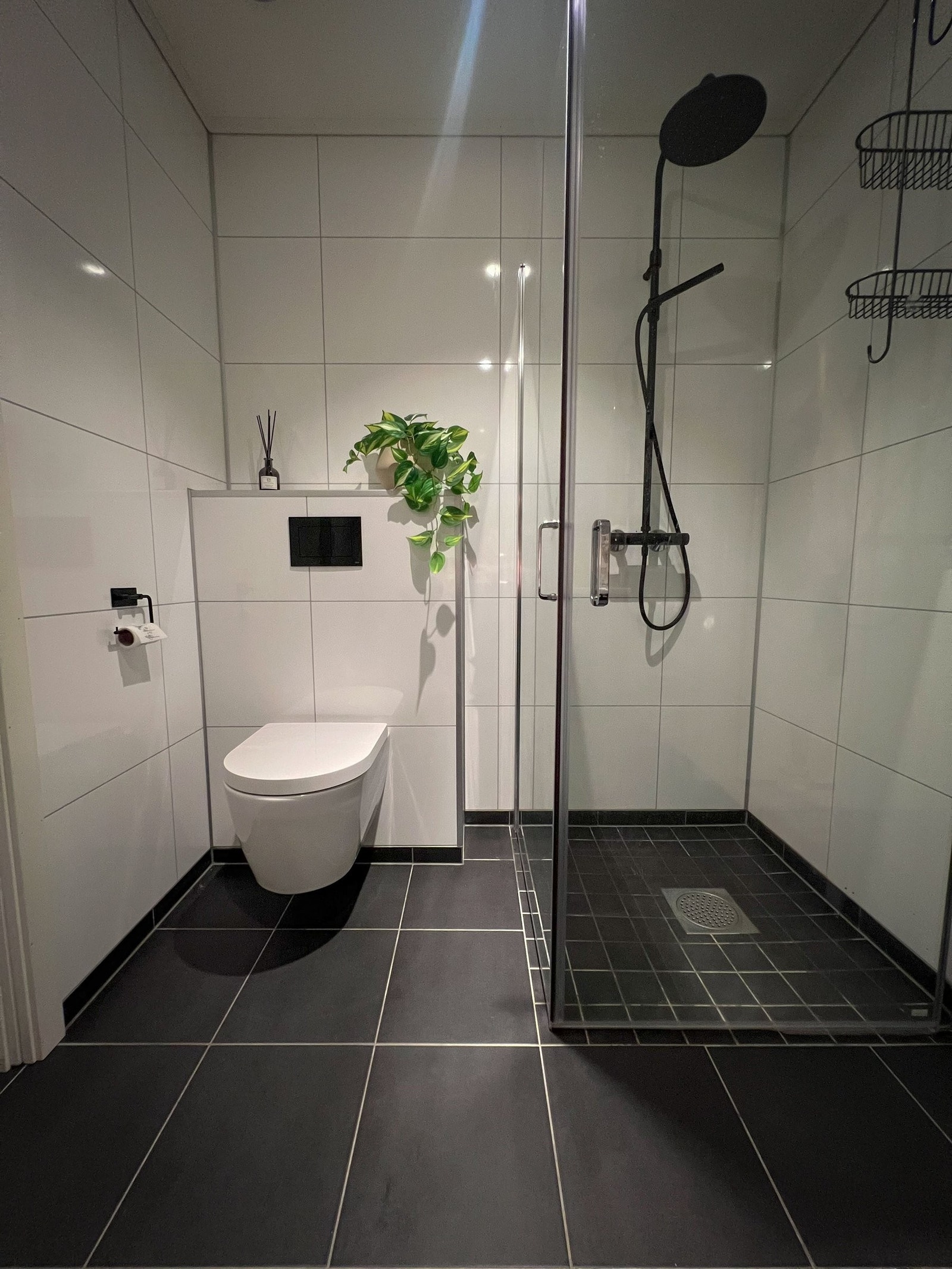 Moderne baderom med dusjhjørne i glas, vegghengt toalett og delikate, mørke golvfliser. Reint uttrykk og praktiske løysingar som gir eit stilfullt og funksjonelt bad. Galleribilde