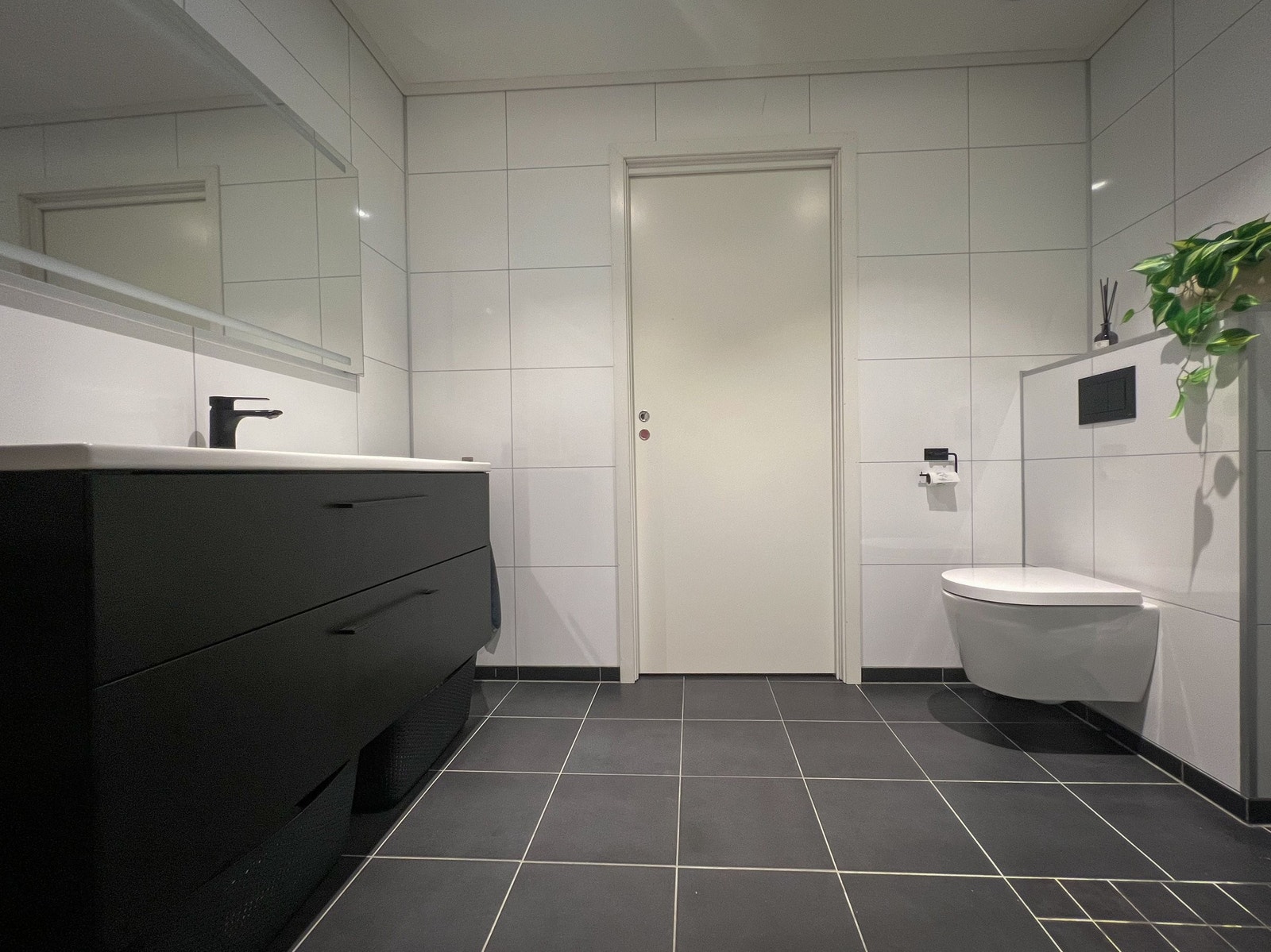 Lyst og moderne baderom med tidlaust flisvalt, vegghengt toalett og romsleg servantløysing med rikeleg oppbevaring. Galleribilde