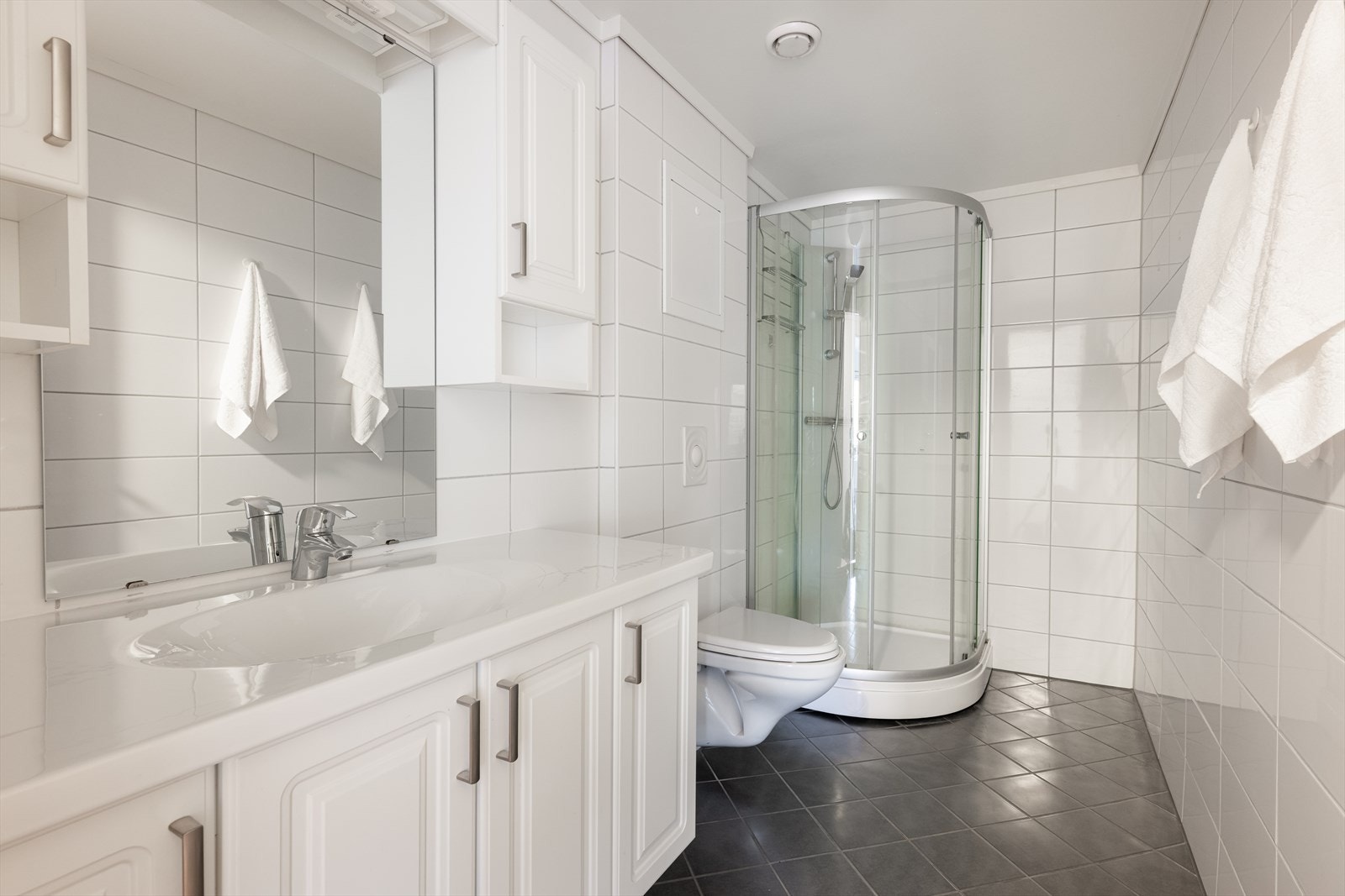 Lyst, helfliset bad med varmekabler i gulvet. God oppbevaringsplass i innredning med heldekkende servant og speil med overlys. Badet er også innredet med dusjkabinett og veggmontert toalett. Totalrenovert i regi av borettslaget i 2015. Galleribilde