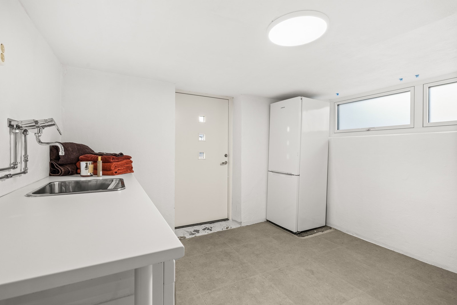 Praktisk vaskerom med egen utgang direkte til terreng. Gulvfliser med gulvvarme. Opplegg for både vaskemaskin og tørketrommel under benkeplaten Galleribilde