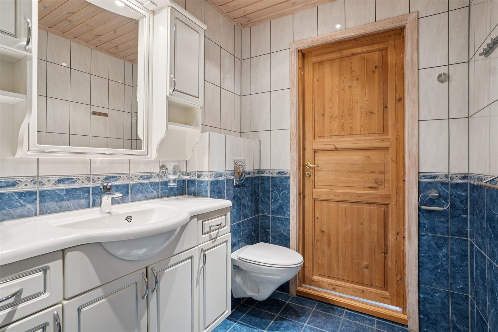 Badet i u.etg. er innredet med skjermet dusjhjørne, vegghengt toalett, servantinnredning, speil på vegg over servant. Galleribilde